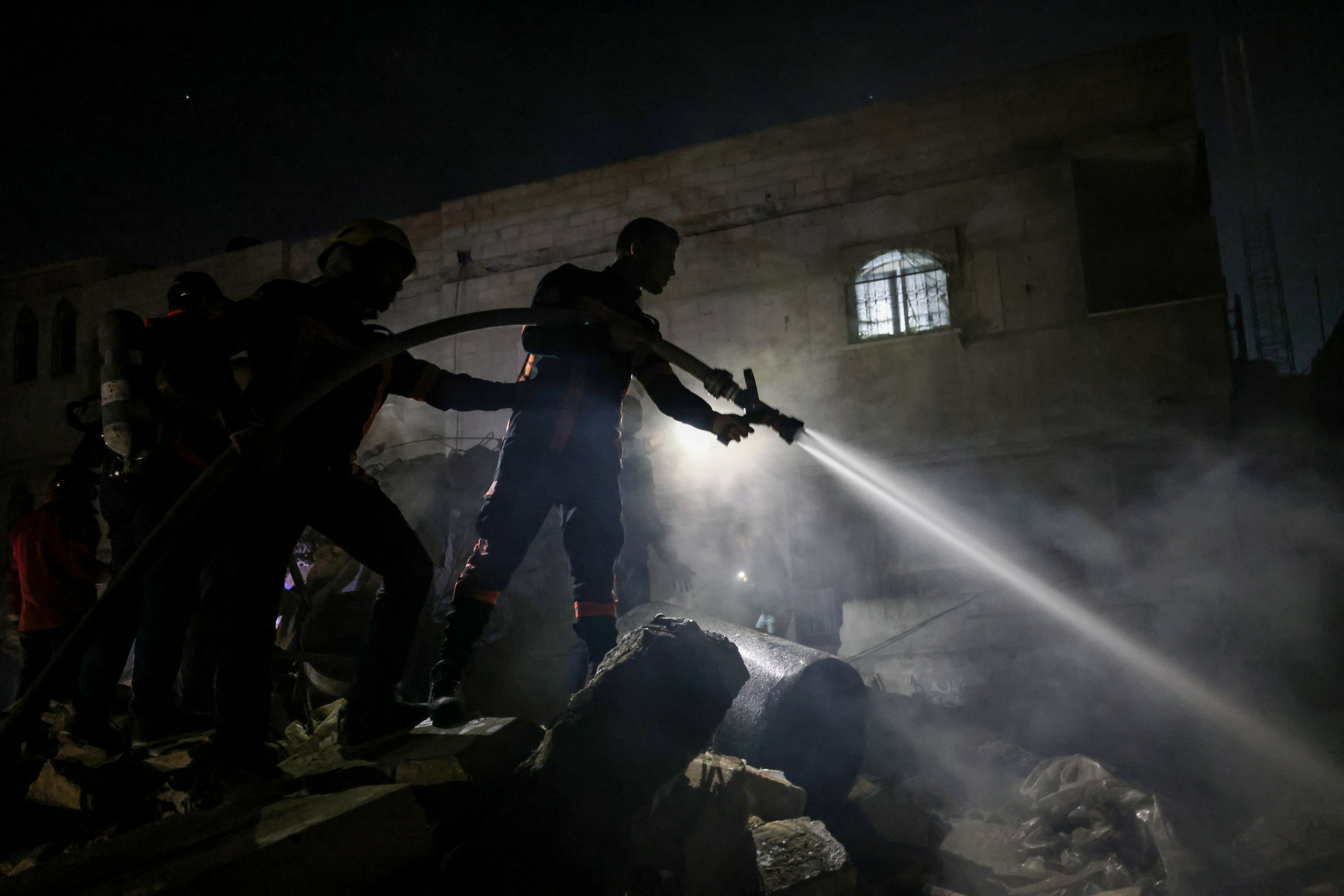 Firefighters spray water on the rubble of a building following Israeli bombardment in Rafah, in the southern Gaza Strip, on December 18, 2023, amid continuing battles between Israel and the Palestinian militant group Hamas. (Photo by MOHAMMED ABED / AFP)