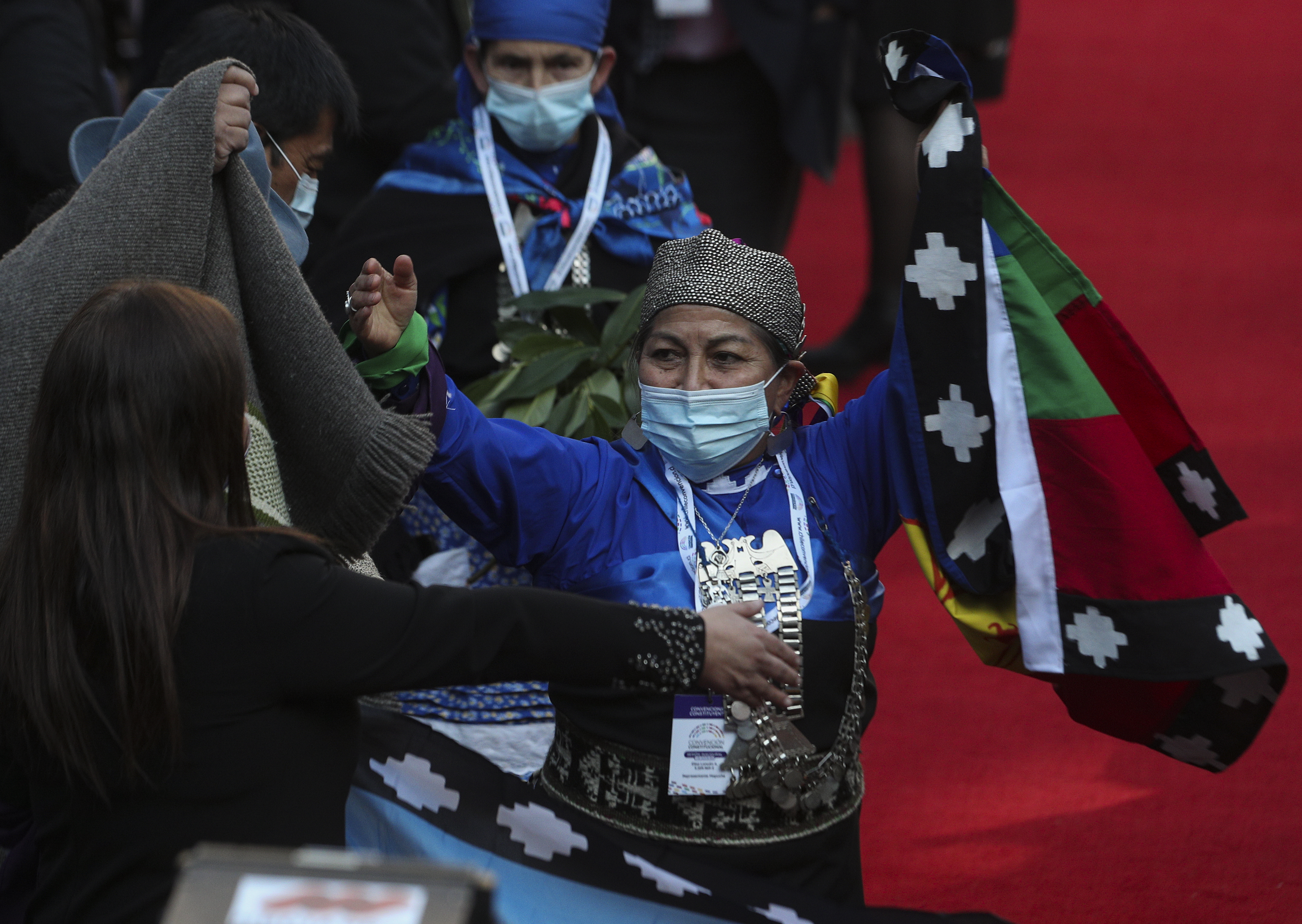 A Mapuche representative raises her arms as she celebrates her election to the constitutional council in 2022. A red carpet is visible behind her, and in one hand she carries a flag.