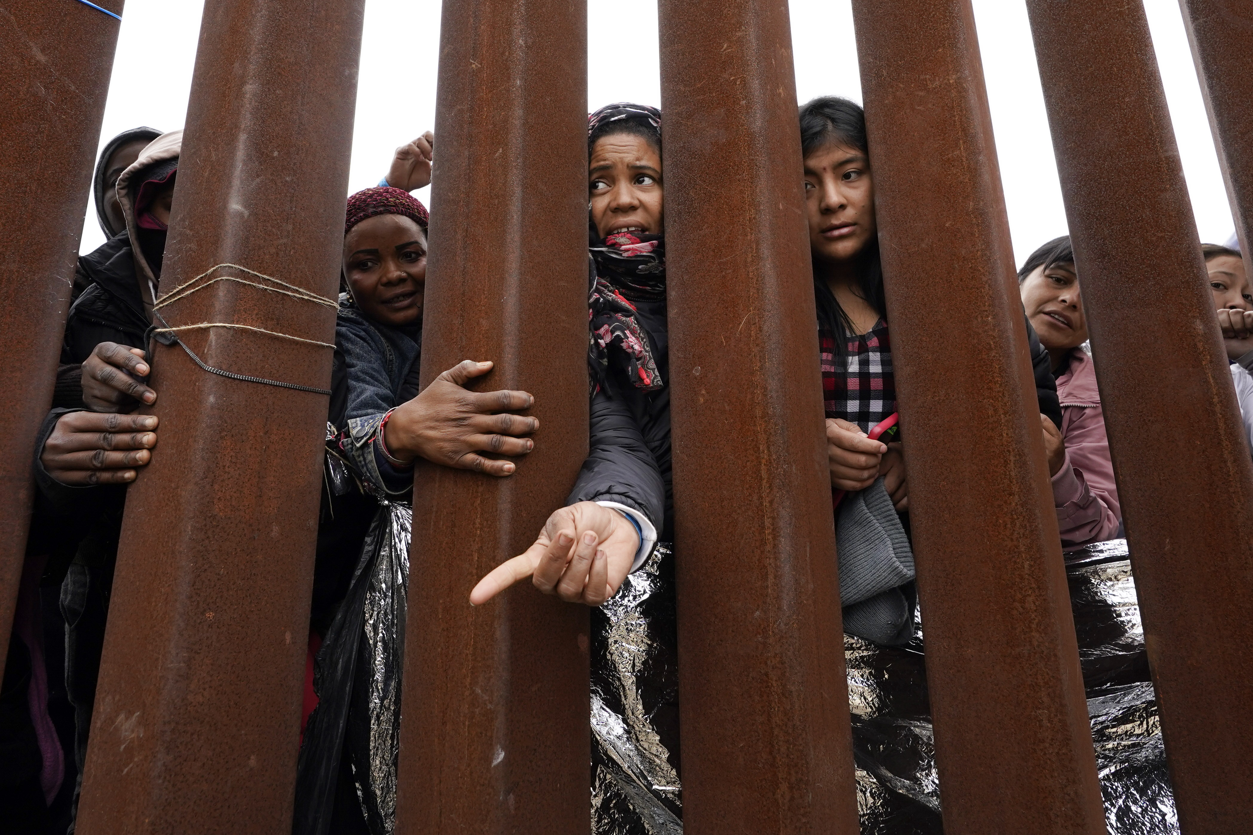 Migrants reach through a border wall for clothing handed out by volunteers, as they wait between two border walls to apply for asylum Friday, May 12