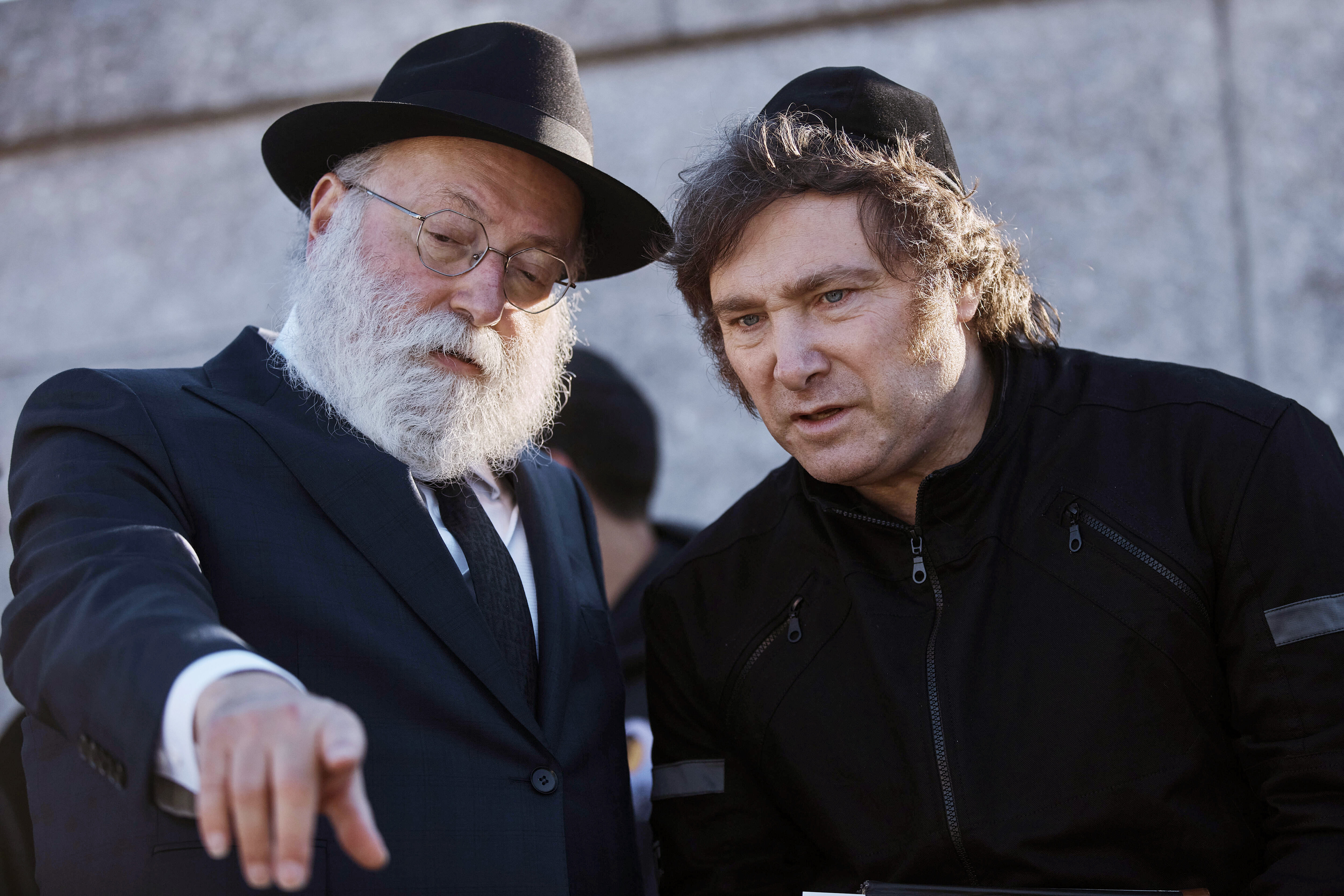 Javier Milei, wearing a black yarmulke, speaks to a rabbi who points to something in front of them.