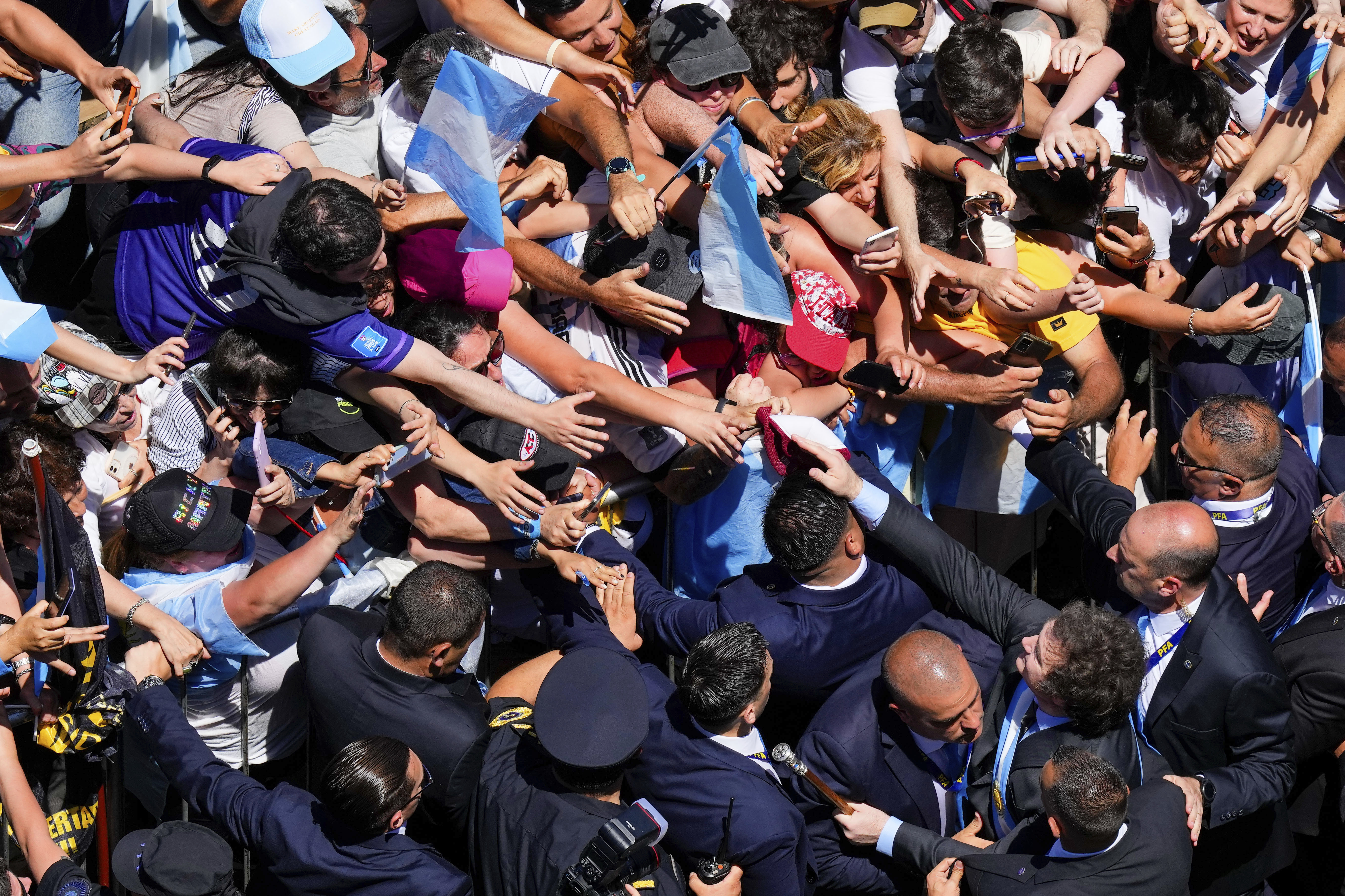 A crowd of supporters reaches towards Javier Milei — many waving Argentine flags — and he reaches back, from across a line of security personnel.