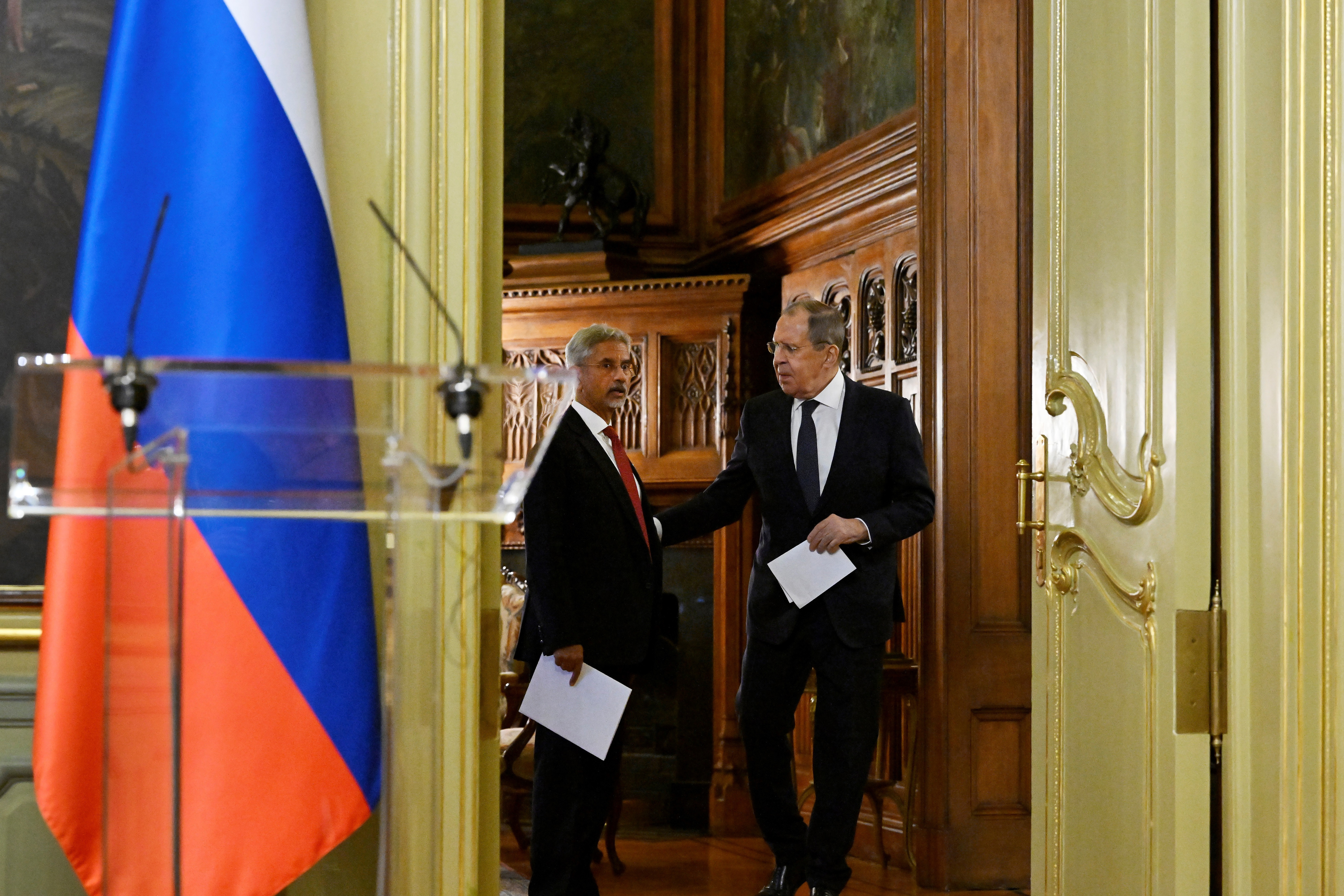 Russia's Foreign Minister Sergey Lavrov, right, and India's Foreign Minister Subrahmanyam Jaishankar arriving for a press conference in Moscow. They are each holding papers. There is a Russian flag and a lectern to the left. 