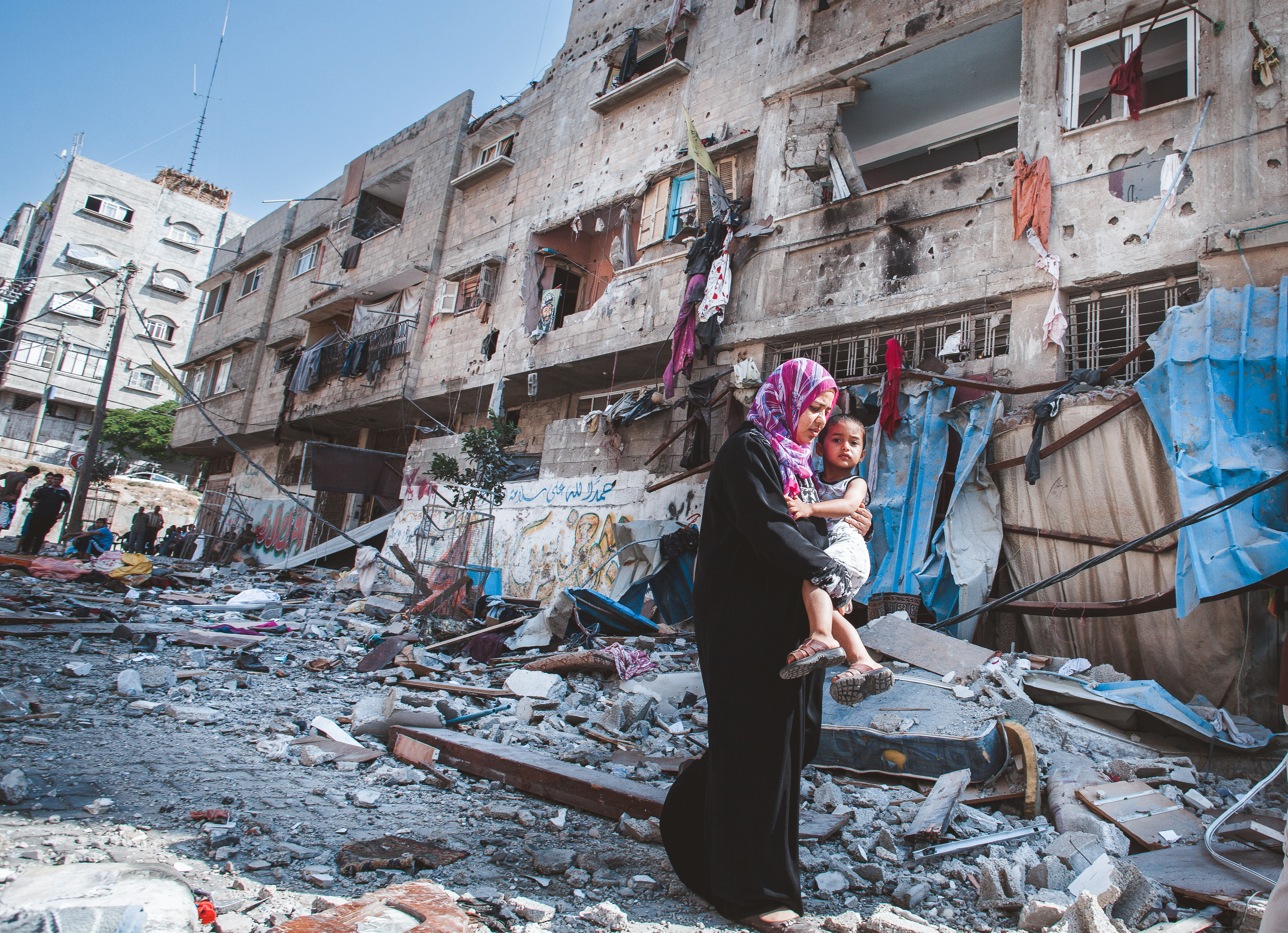 A Palestinian mother holds her son while passing a severely damaged residential building that was destroyed overnight by an Israeli airstrike at Al Sheikh Redwan in Gaza City on July 10, 2014 [Courtesy of Eman Mohammed]
