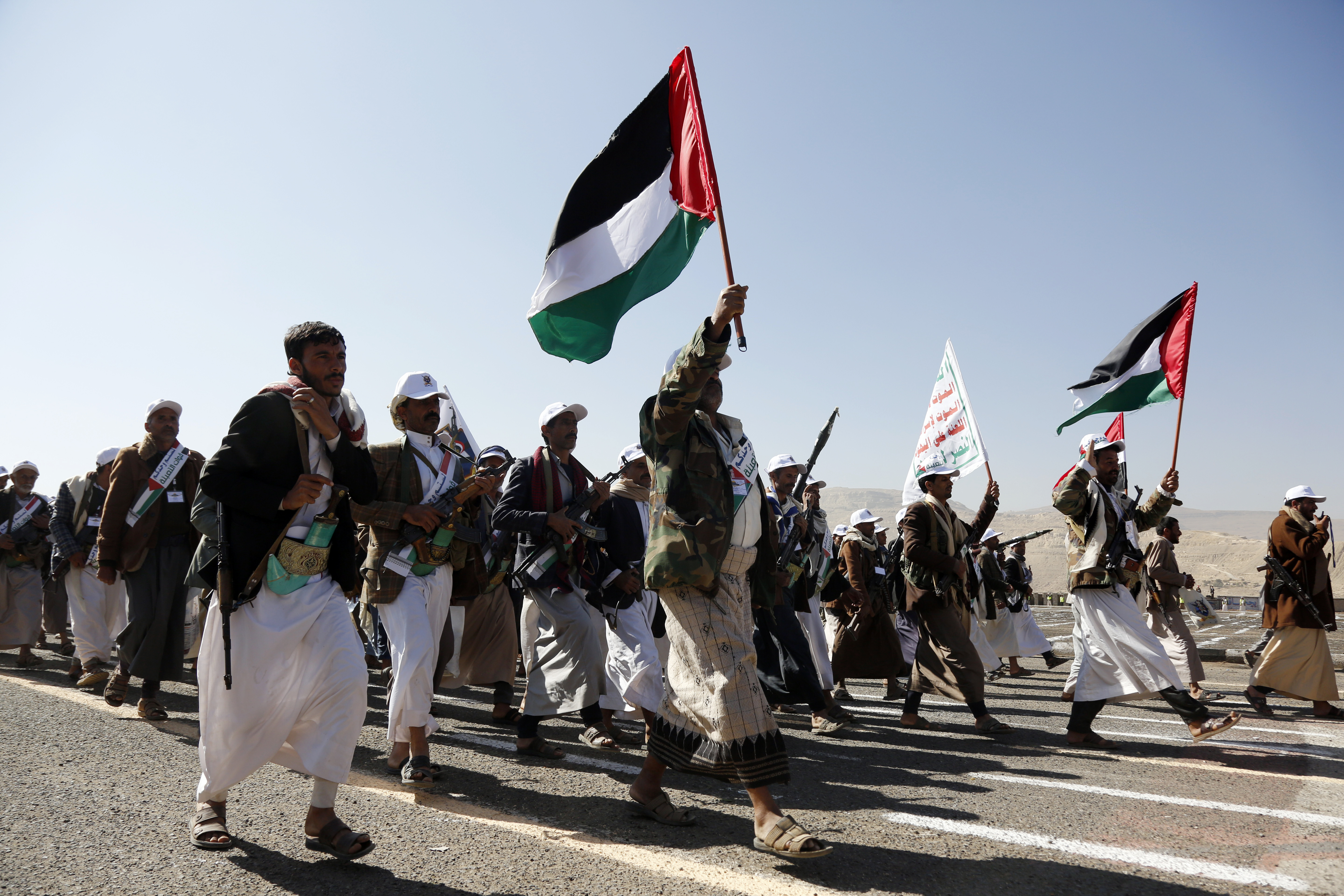men wearing white wave palestinian flags and walk in formation