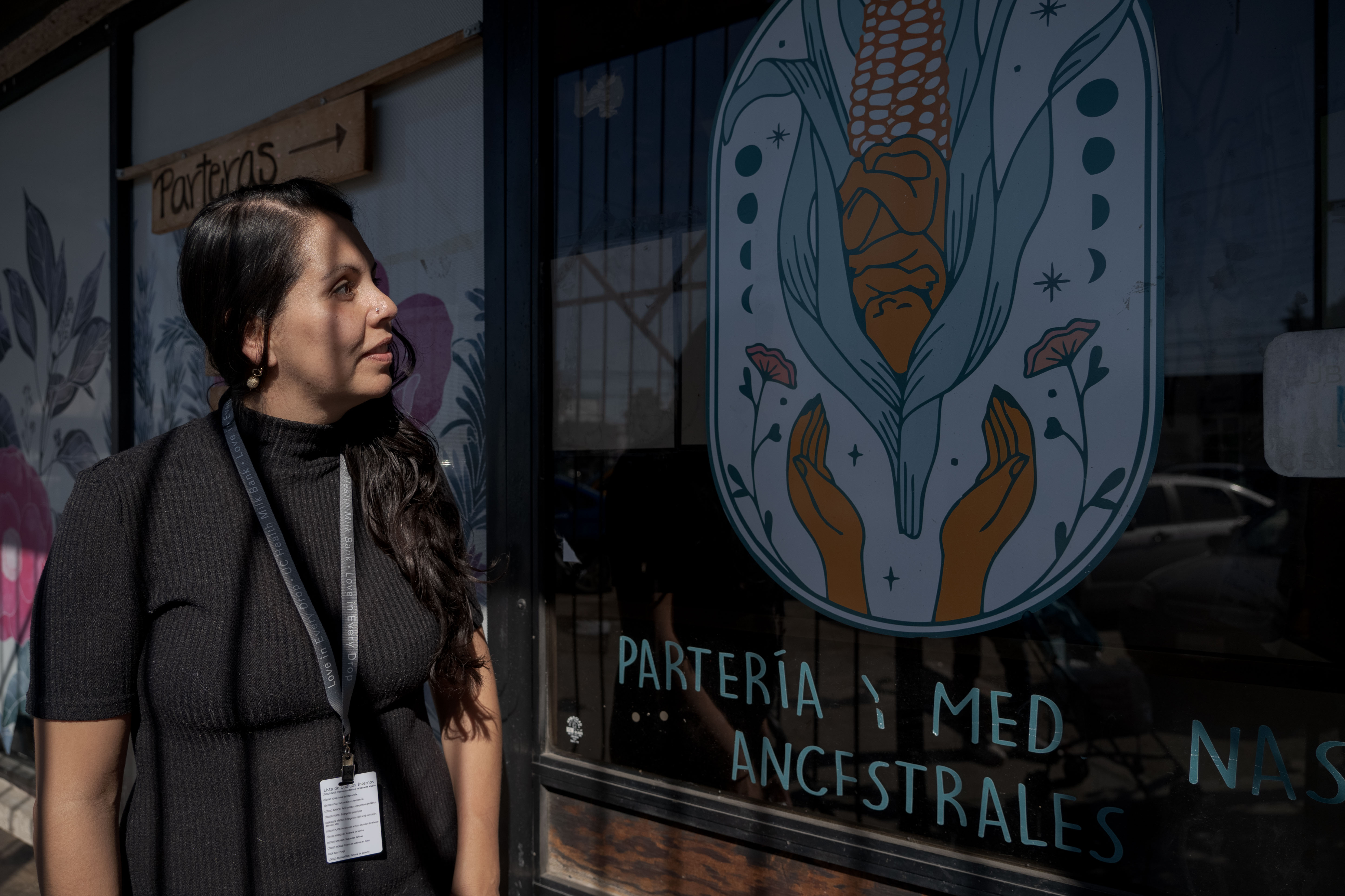 A woman in a black T-shirt looks up at a window with a painted logo, advertising services for migrant women.