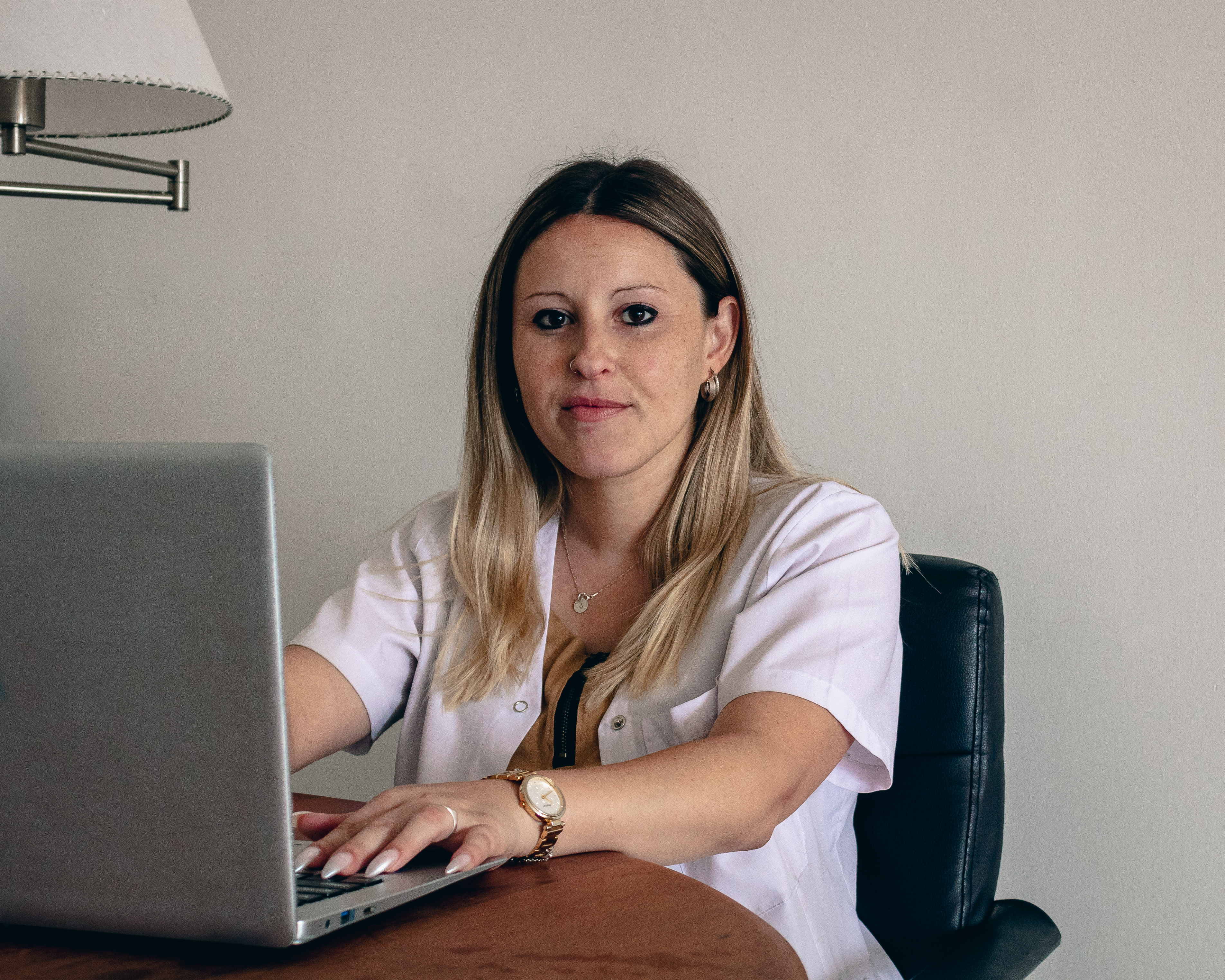 A blonde woman sits at her computer, which is perched on a wooden table.