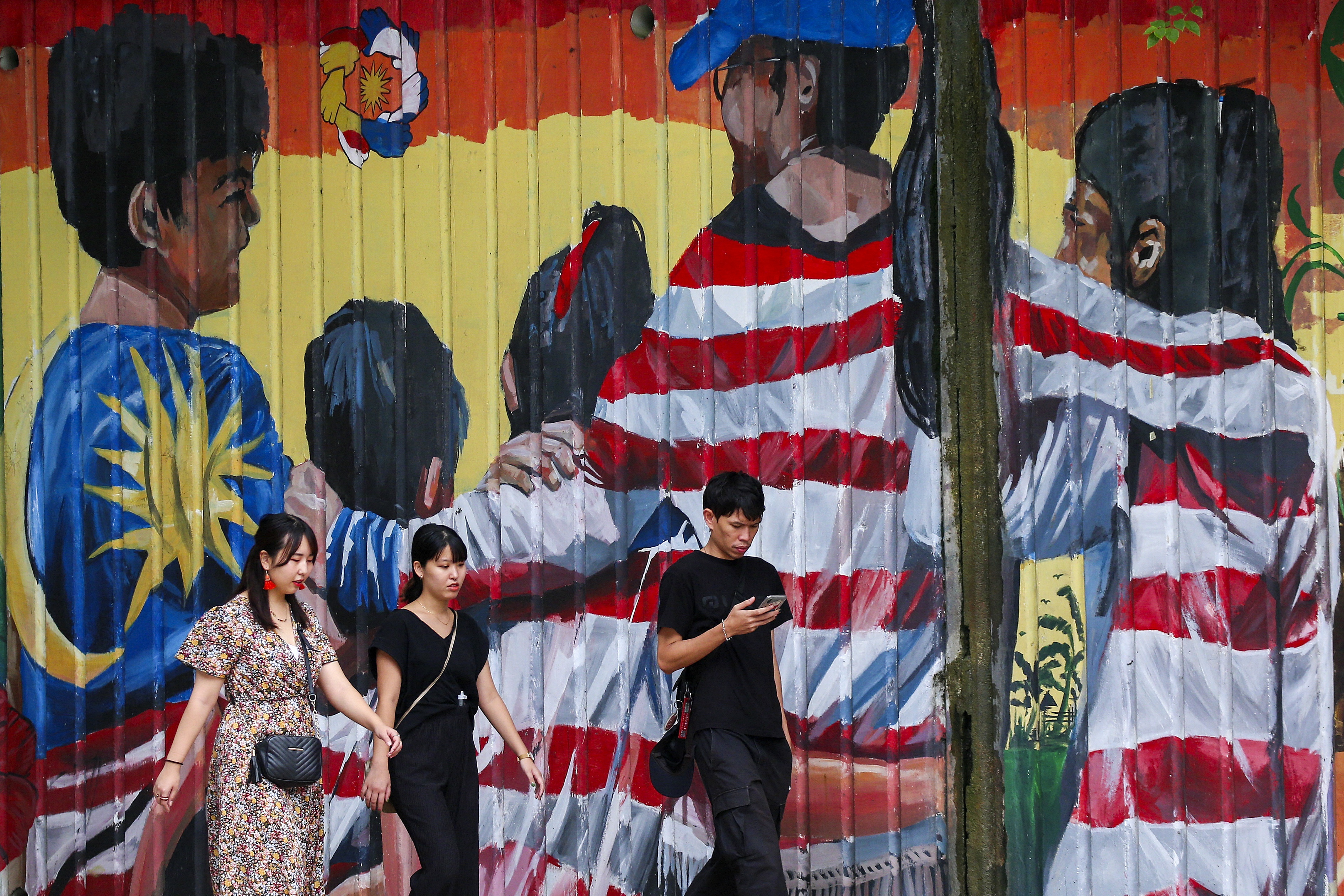 People walking in front of a wall painted with the Malaysian flag