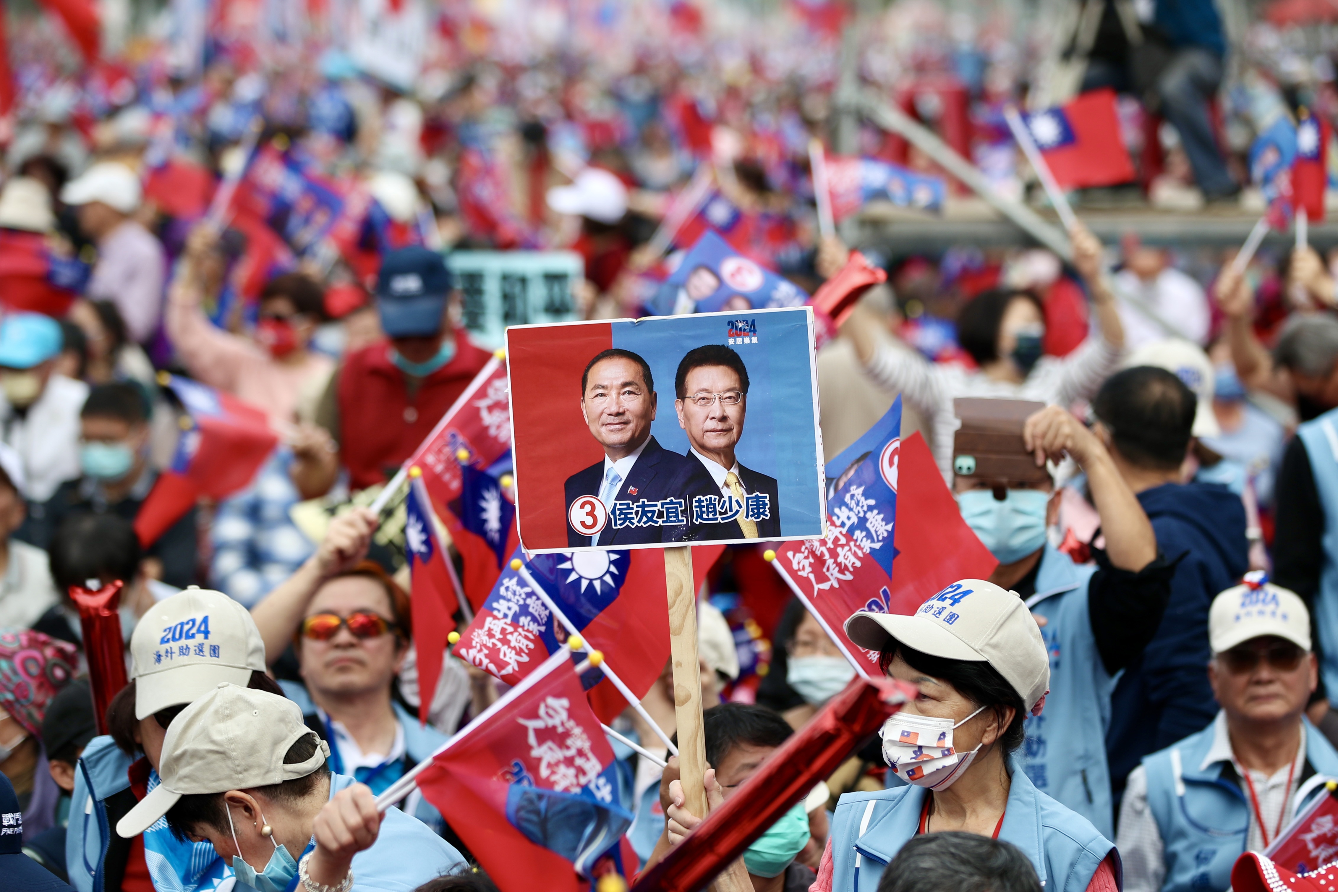 A crowd of people at a KMT rally. They are waving flags and holding placards of their candidates.