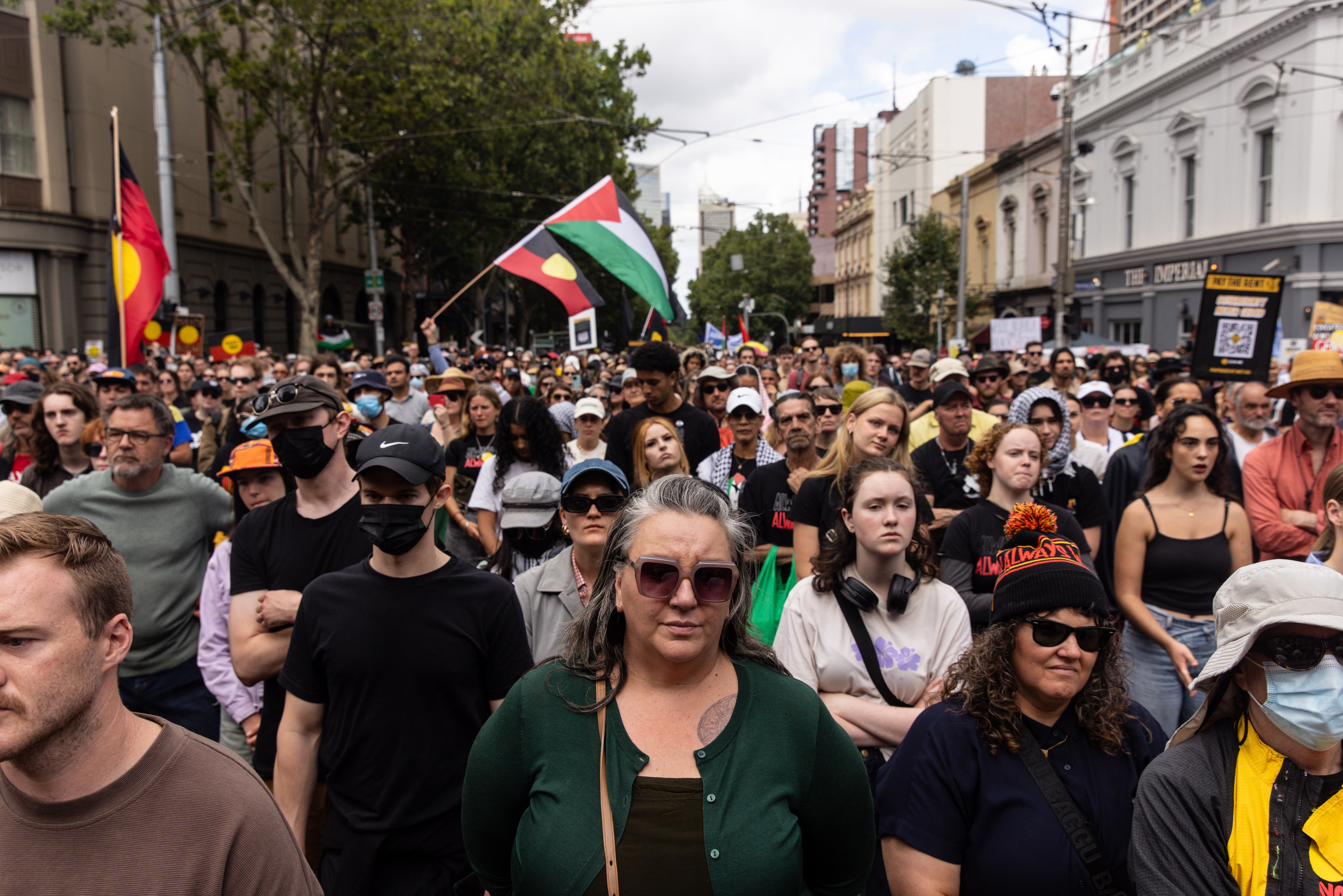 A crowd of protesters in Melbourne at an Invasion Day rally. They are carrying Aboriginal flags