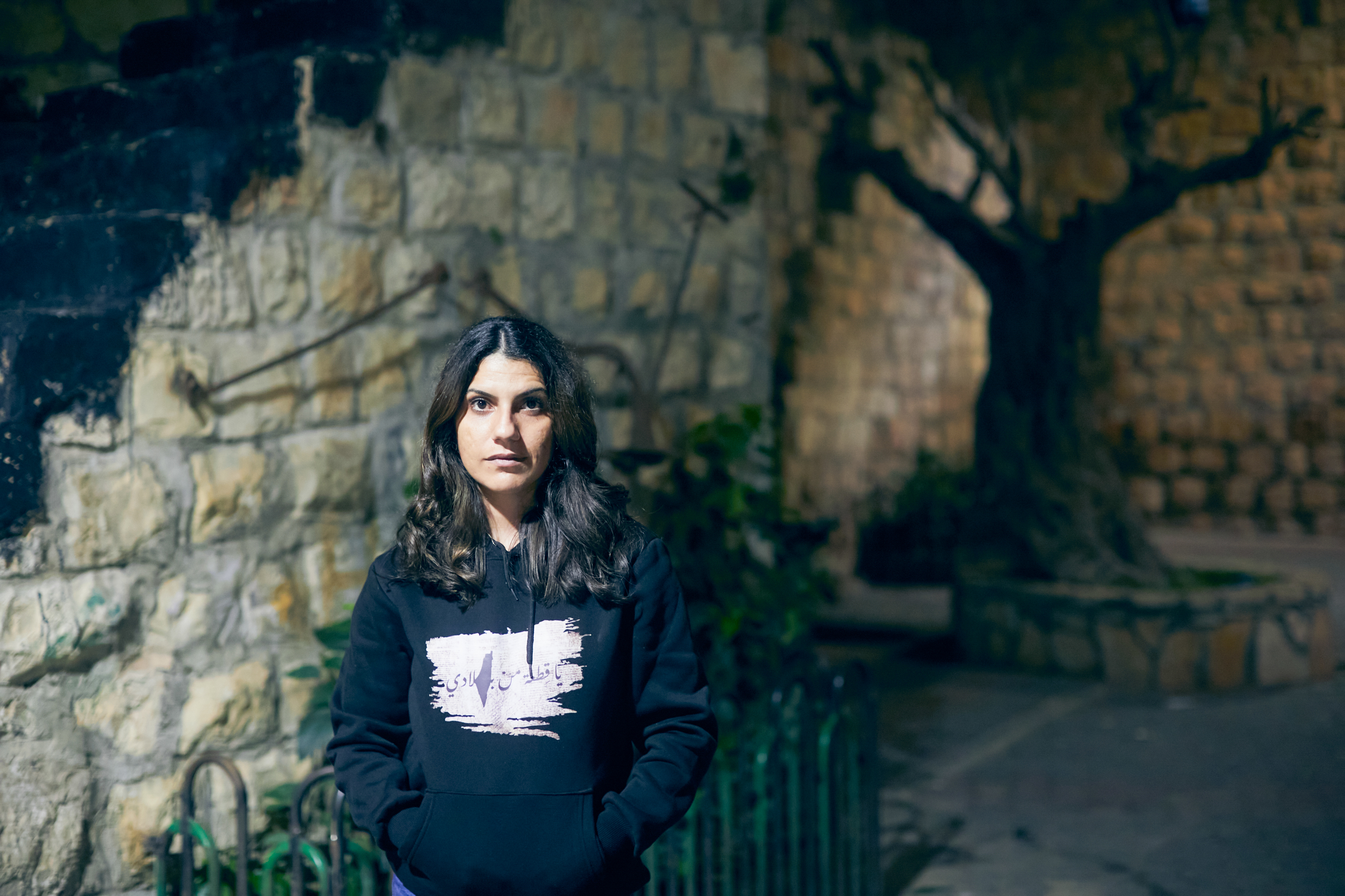 Nour in dark sweatshirt standing in a sone house