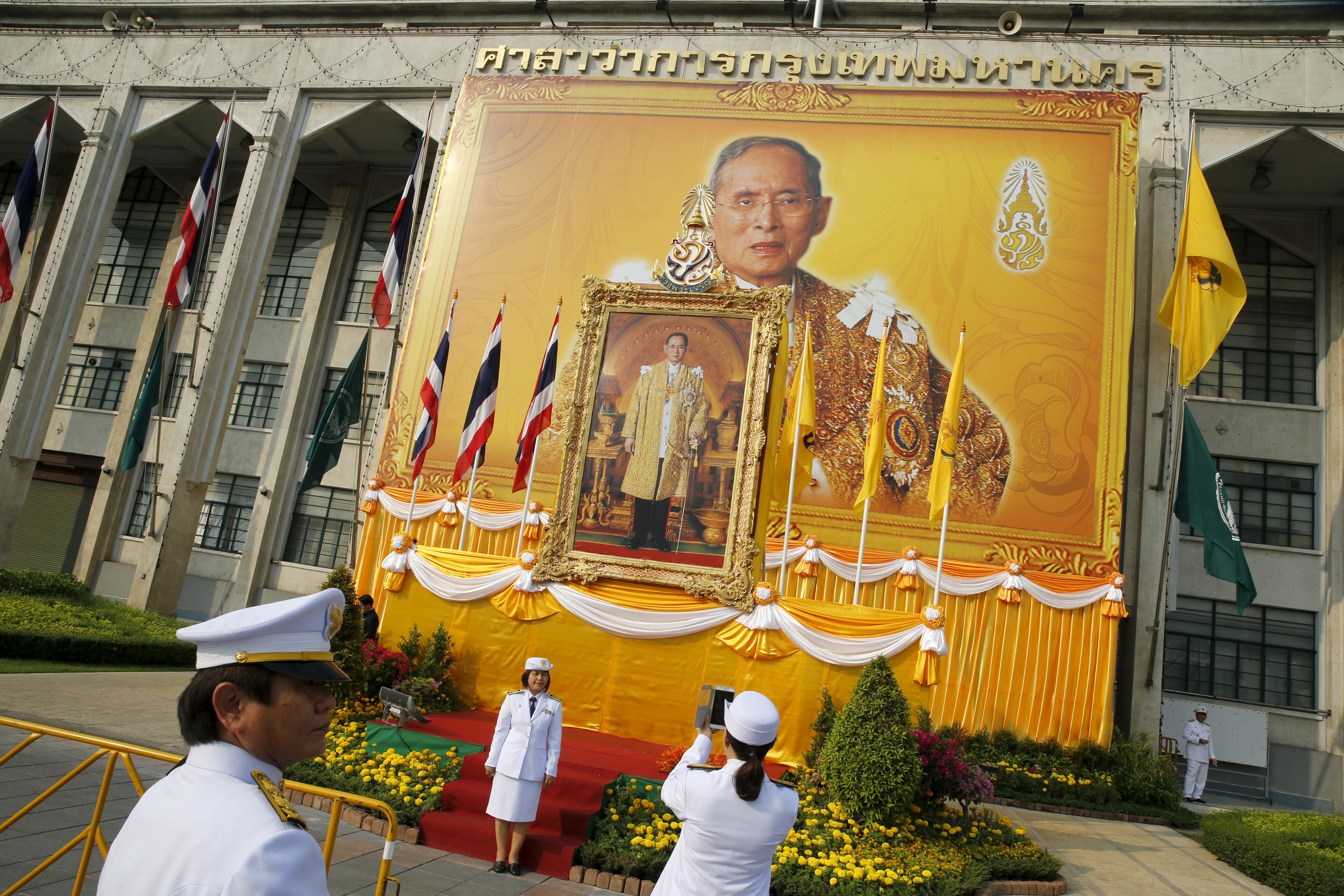 Army officials take pictures in front of a Thai King Bhumibol Adulyadej portrait as people gather to mark his 88th birthday, in Bangkok December 5, 2015. Thais marked the birthday of King Bhumibol Adulyadej, the world's longest-reigning monarch, early on Saturday, by giving alms at temples around the country. Celebrations in Thailand, where the monarch's birthday is also national Father's Day, come amid a widening police investigation into a group of people charged with insulting the monarchy. The king has spent the past few months at the hospital being treated for hydrocephalus. REUTERS/Jorge Silva