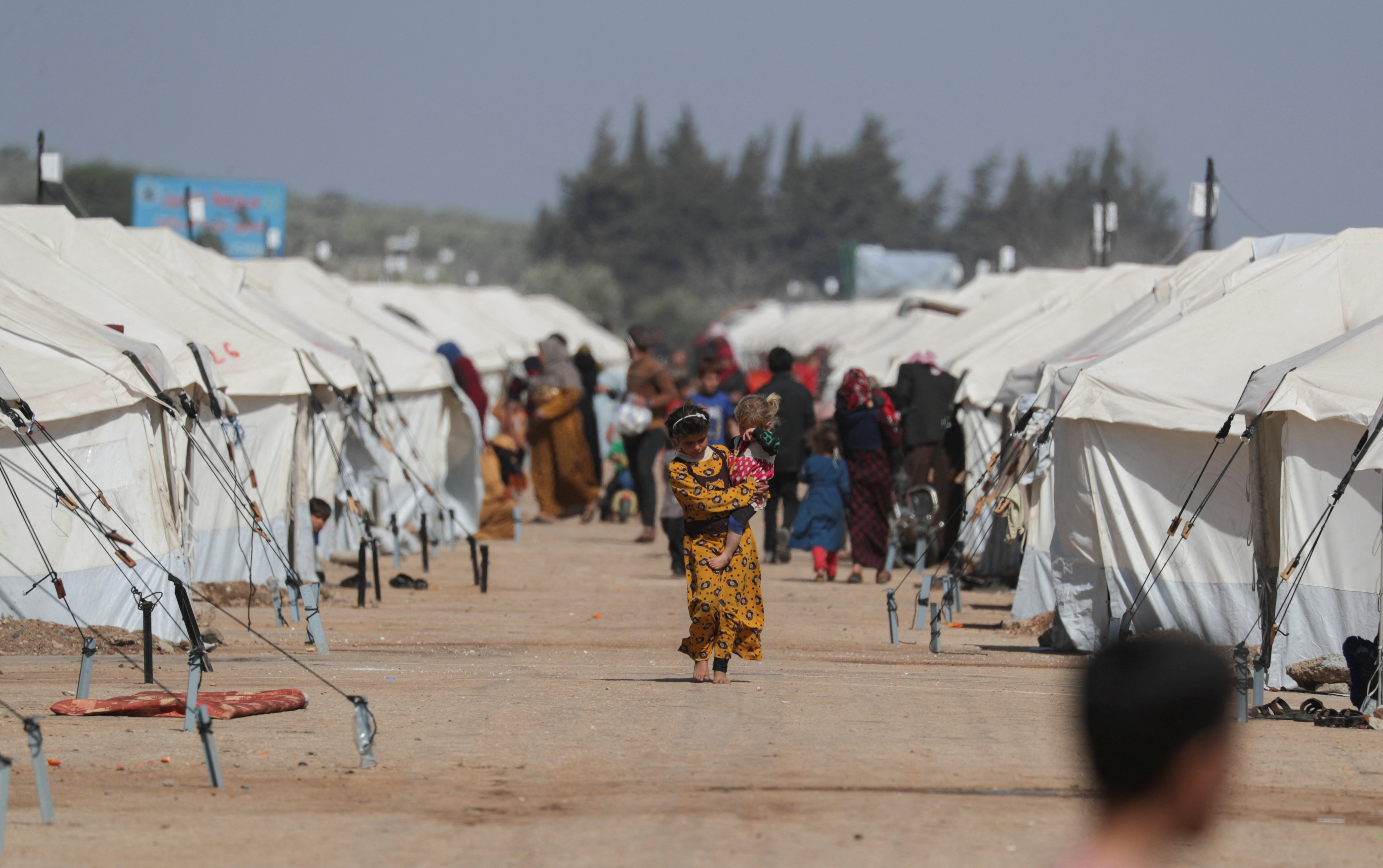 A girl walks as she carries a child past tents erected for the internally displaced following an earthquake, on a land that was previously a driving school, in the rebel-held town of Jandaris, Syria March 4, 2023