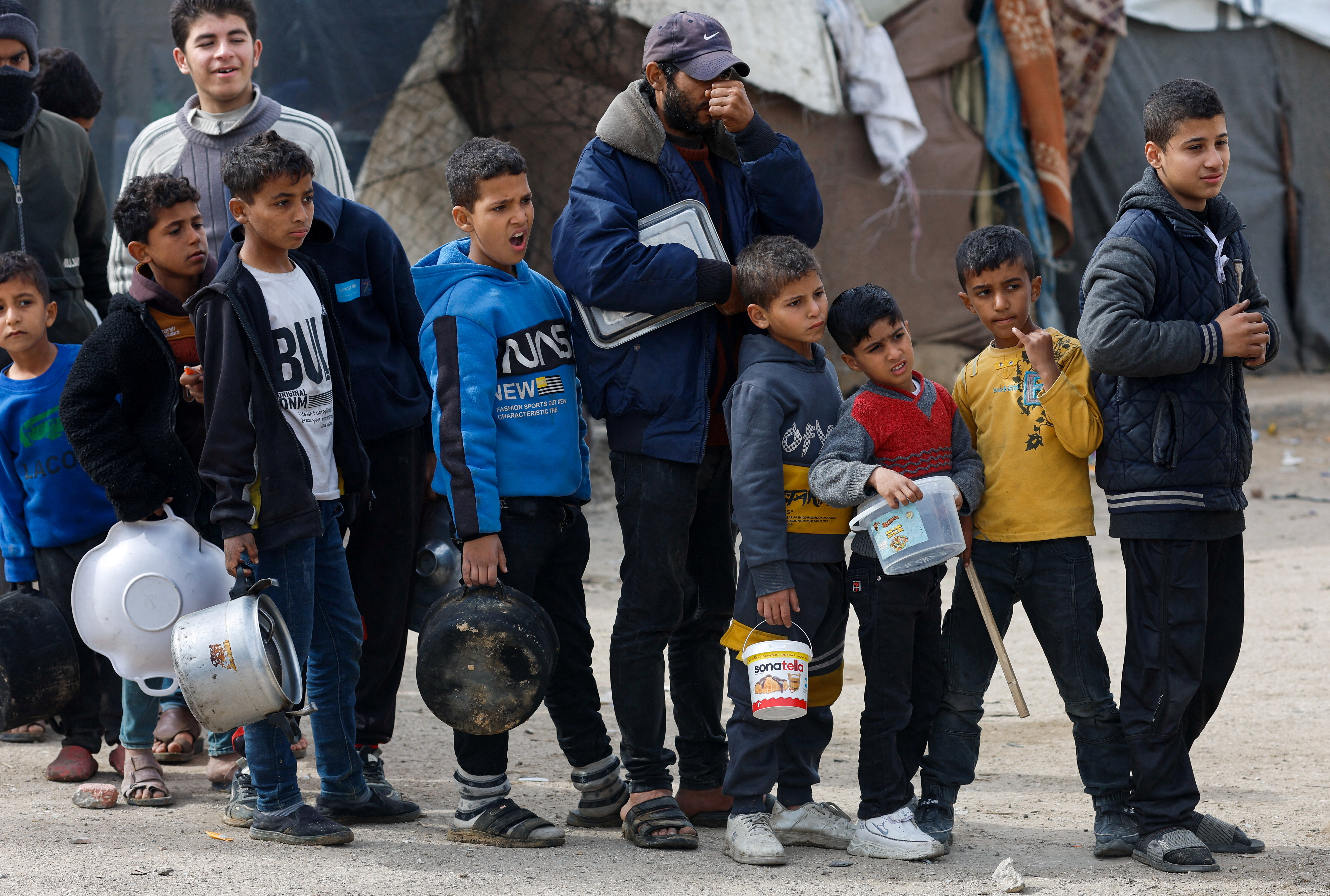Palestinians stand in a line as they wait to receive food amid shortages of food supplies