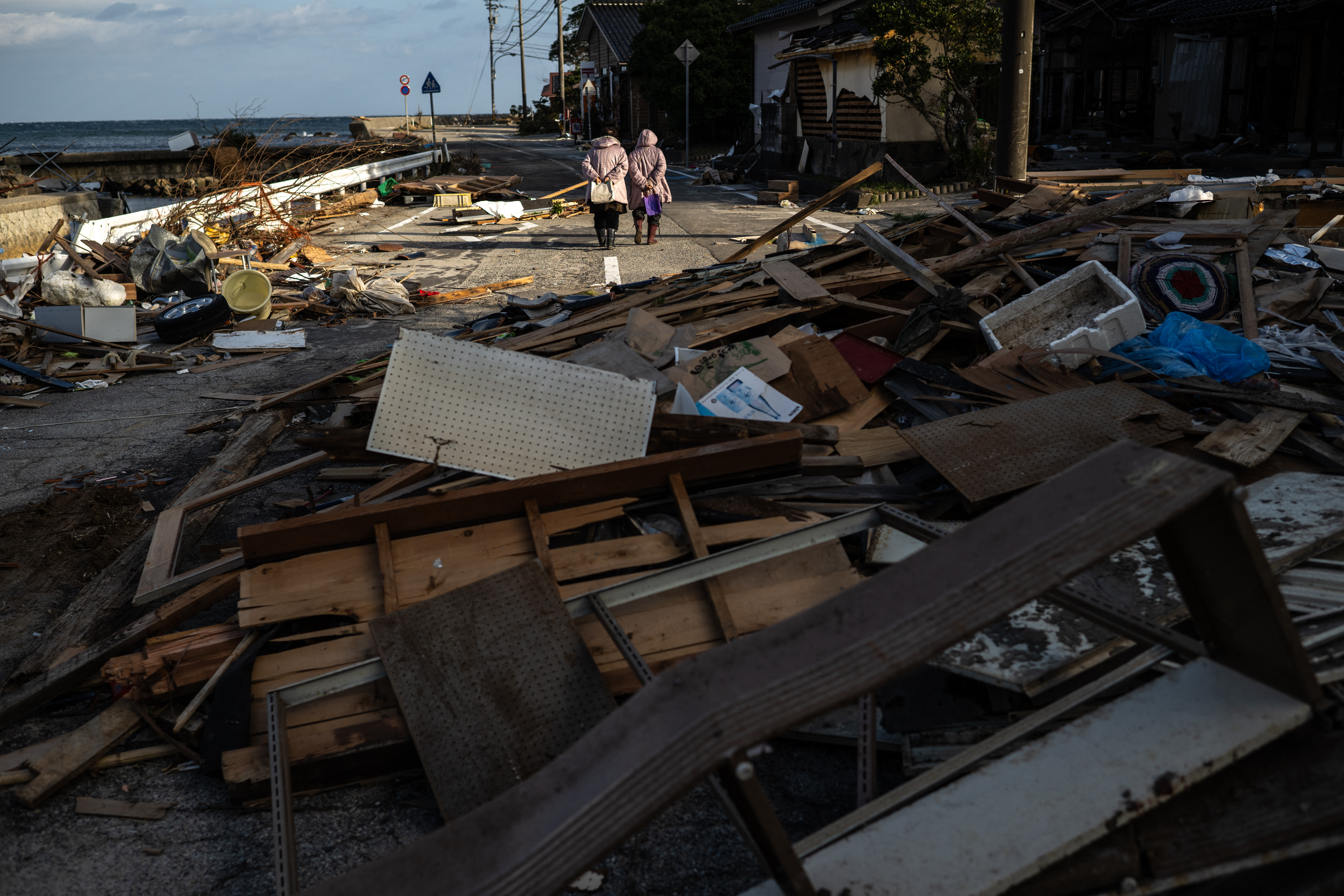 A couple walking into the distance. The road where they are walking is strewn with rubble and debris
