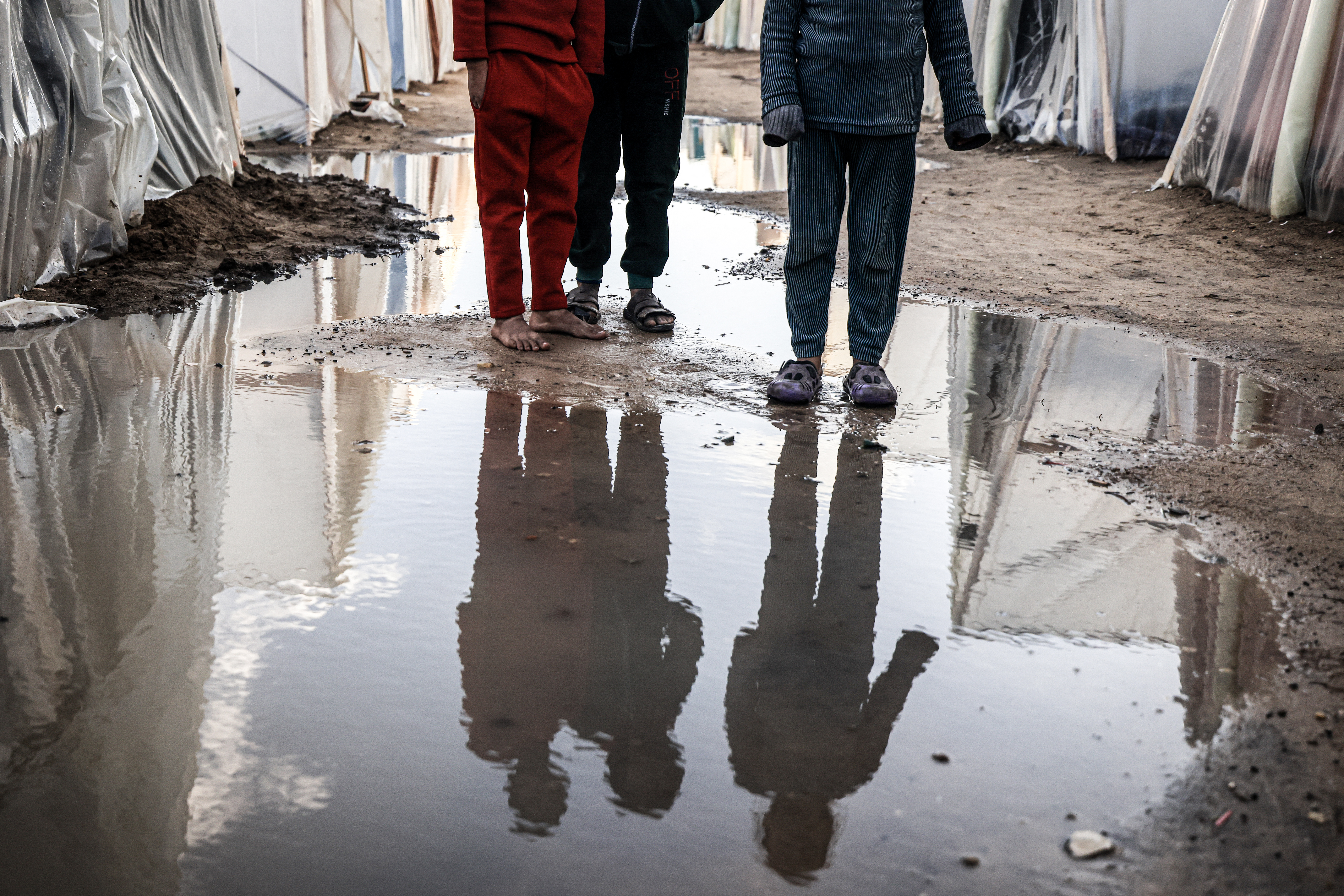Displaced Palestinian children stand amid tents flooded by heavy rain, at a makeshift camp set up by people who fled the ongoing battles between Israel and Hamas militants, in Rafah