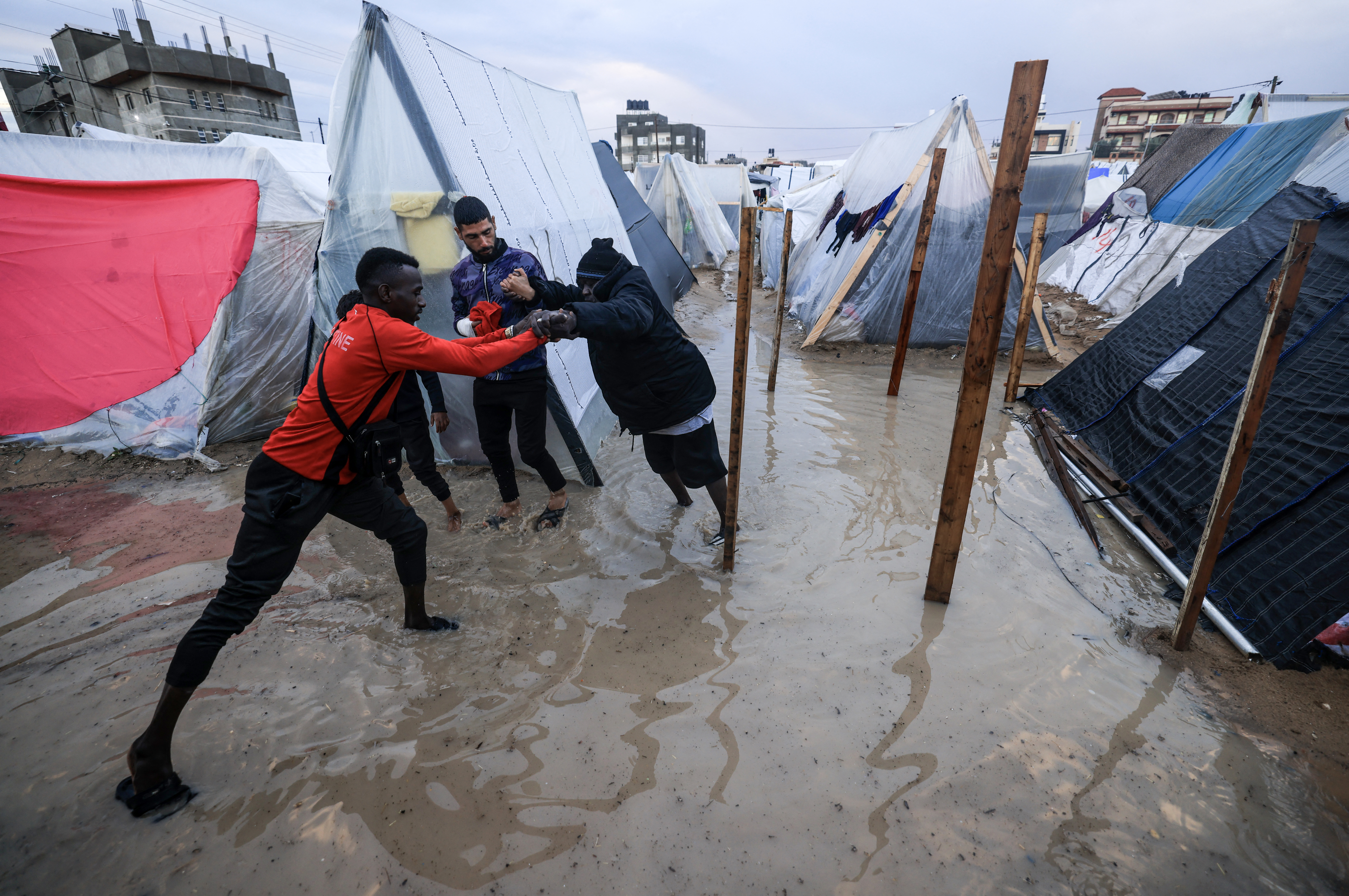 A displaced Palestinian man helps a woman to find her way amid tents flooded by heavy rain, at a makeshift camp set up by people who fled the ongoing battles between Israel and Hamas militants, in Rafah in the southern Gaza Strip on January 27
