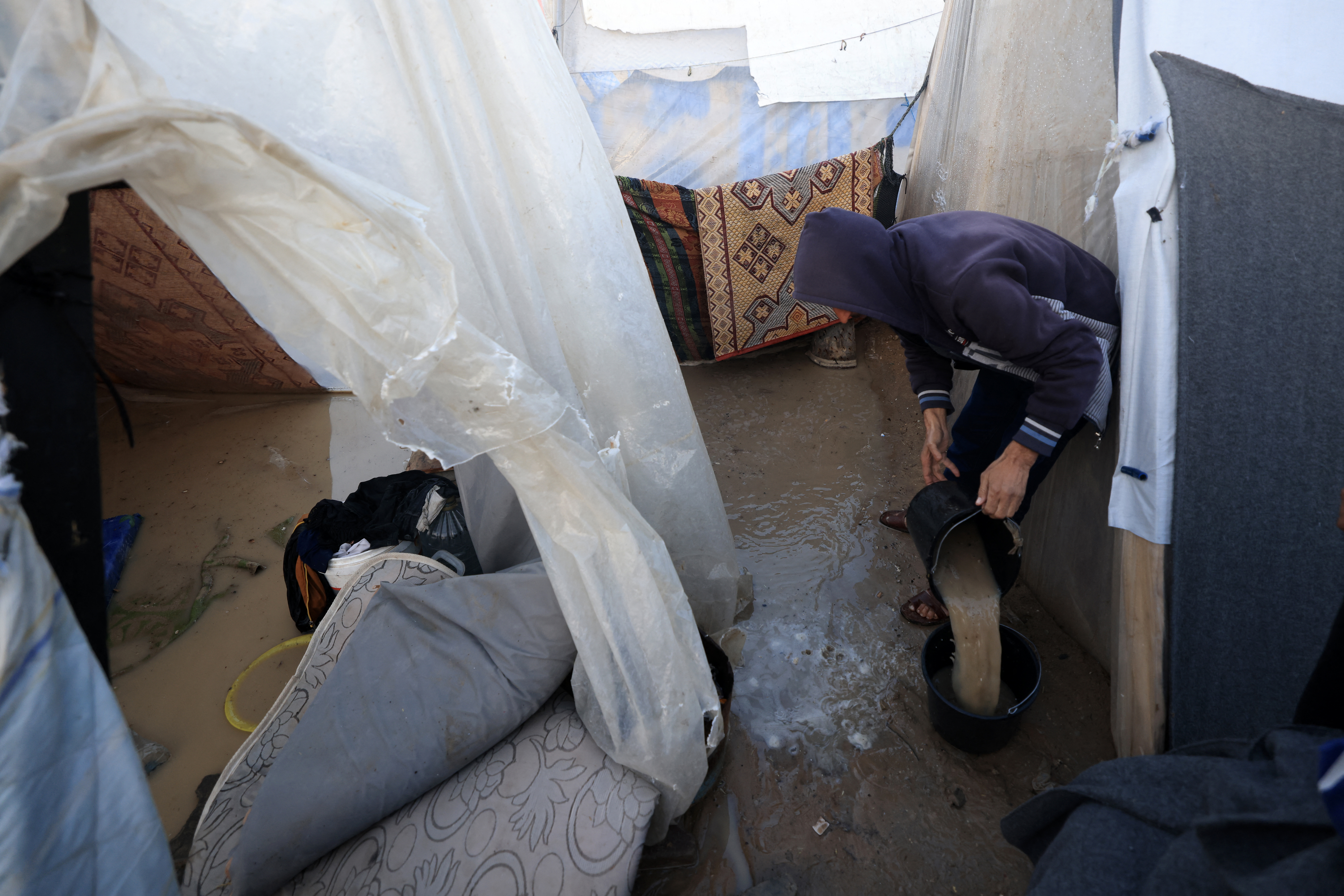 A displaced Palestinian uses a bucket to clear water from a tent drenched by heavy rain, at a makeshift camp in Rafah