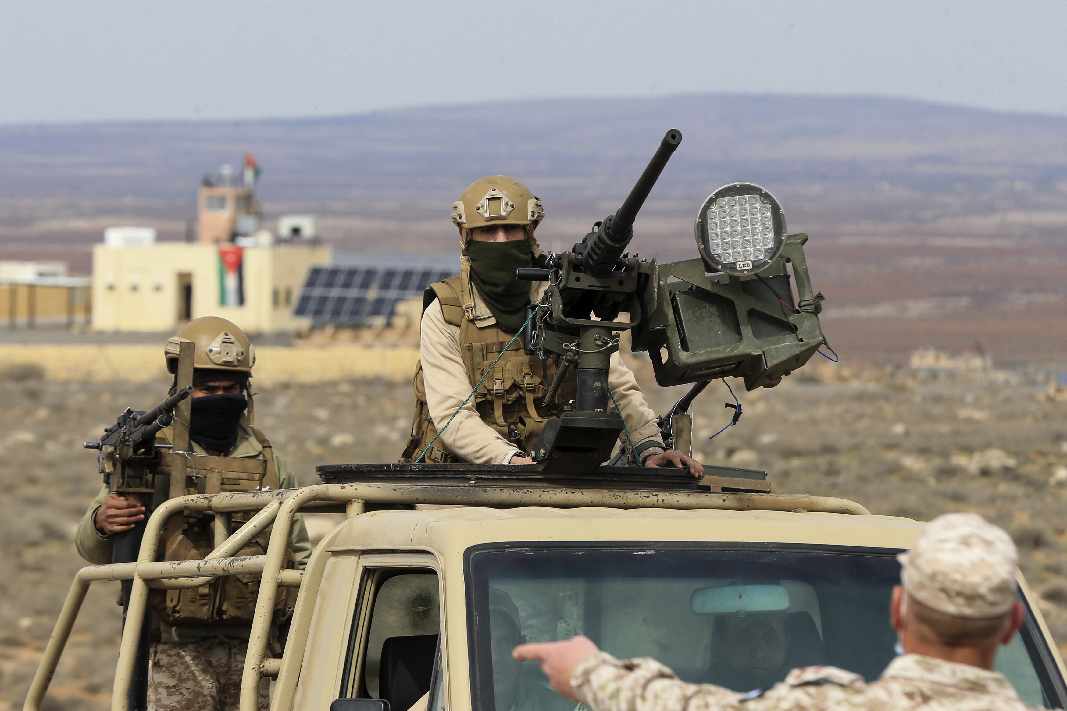 A Jordanian soldier stands in the back of a military truck, behind a mounted machine gun.