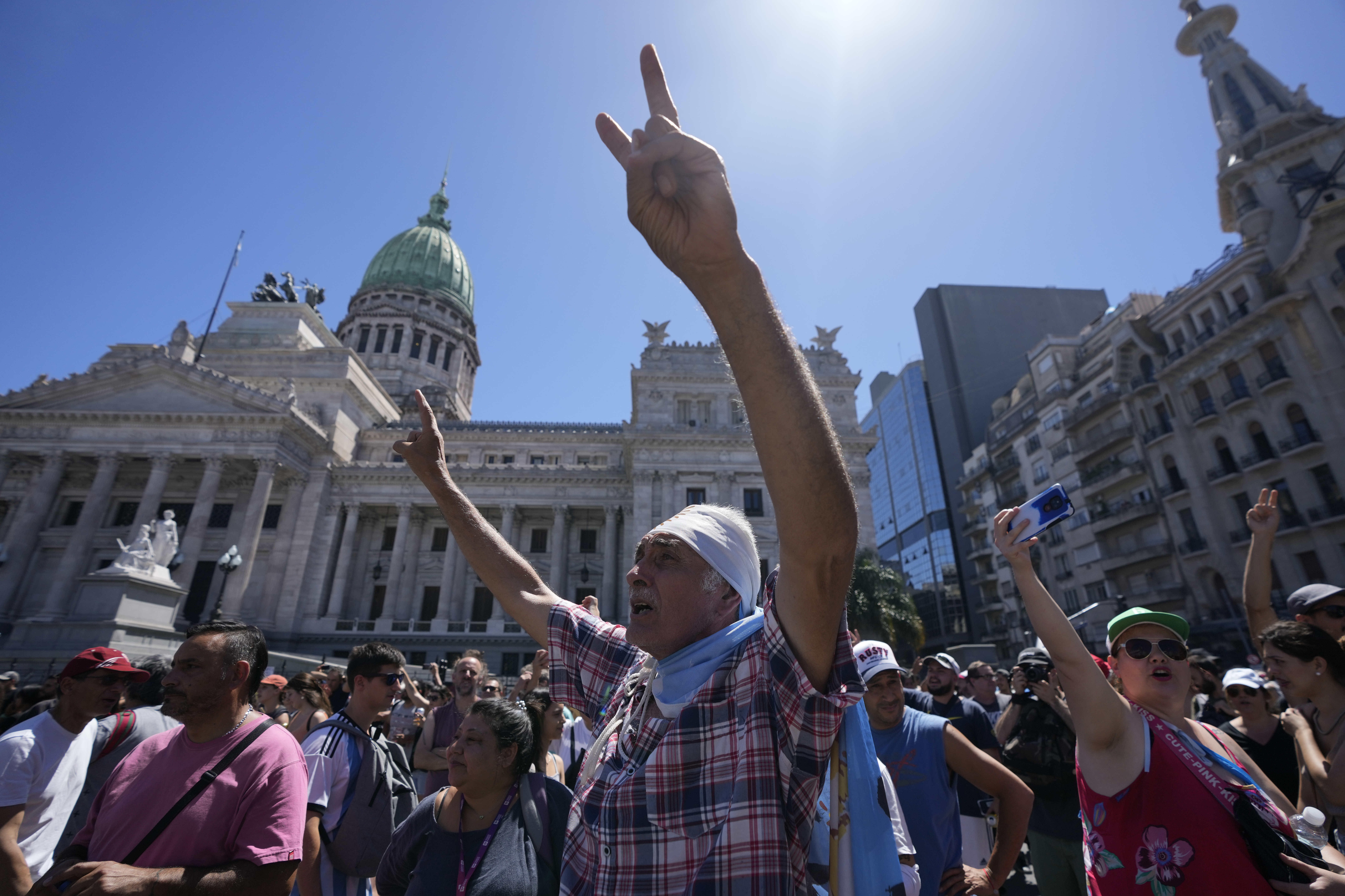 A man lifts his hands into the air, flashing peace signs, as he wears an Argentine flag outside the Congress building in Buenos Aires.