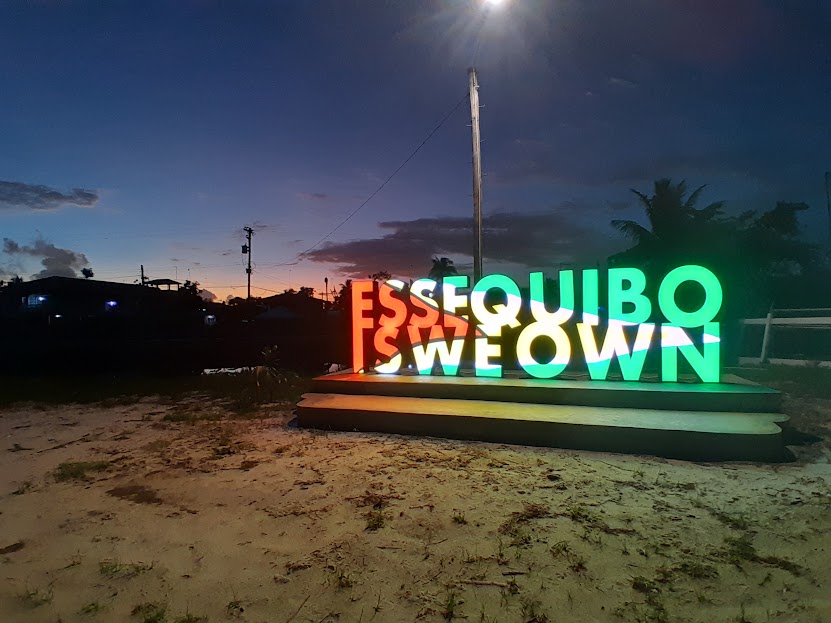 An electric sign, lit up with the colours of the Guyanese flag, says: "Essequibo is we own." Behind the sign is the faint glow of daylight.