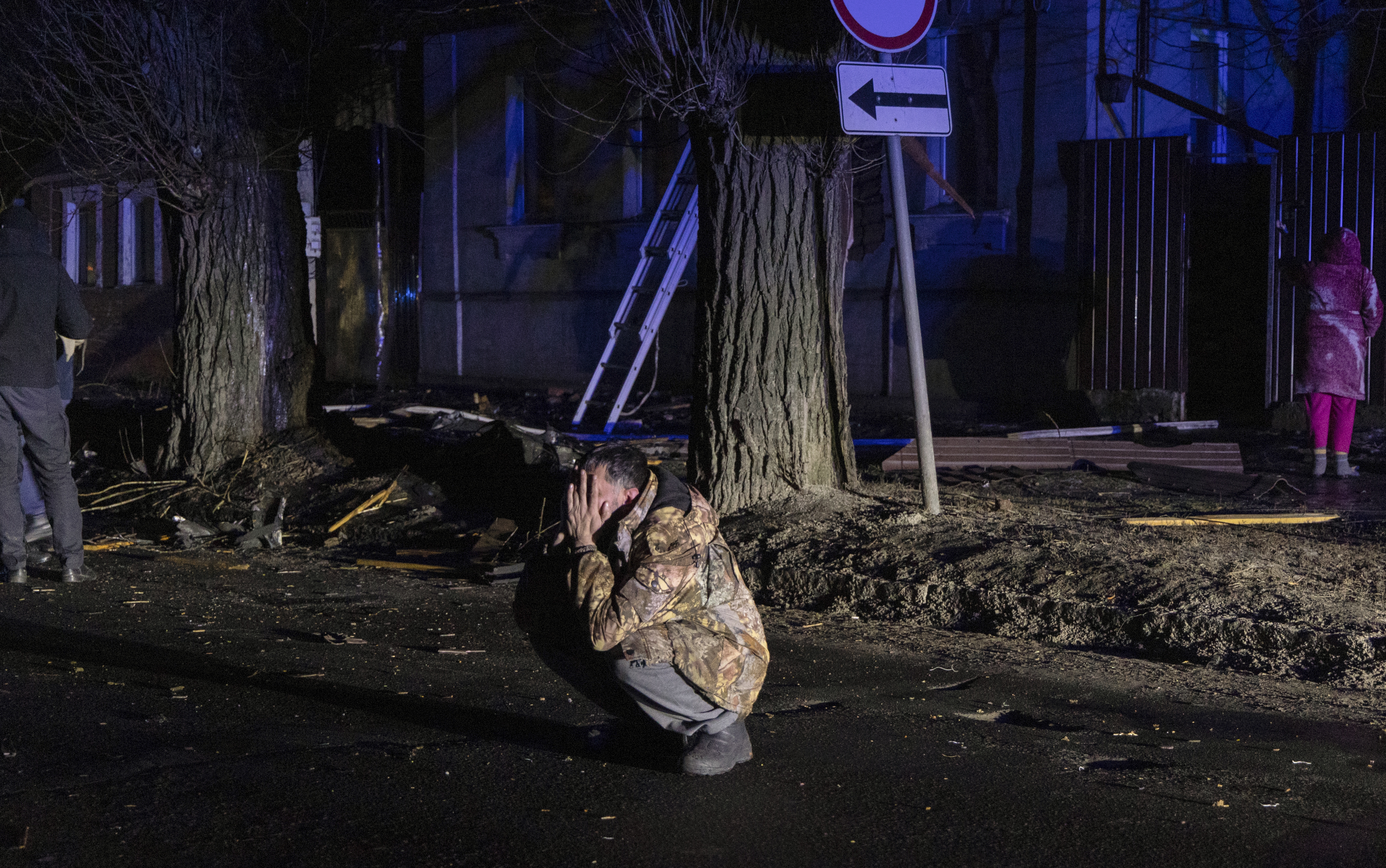 A man squats down and holds his head in his hands after a Russian air attack on Kharkiv. He is out on the street in the darkness.