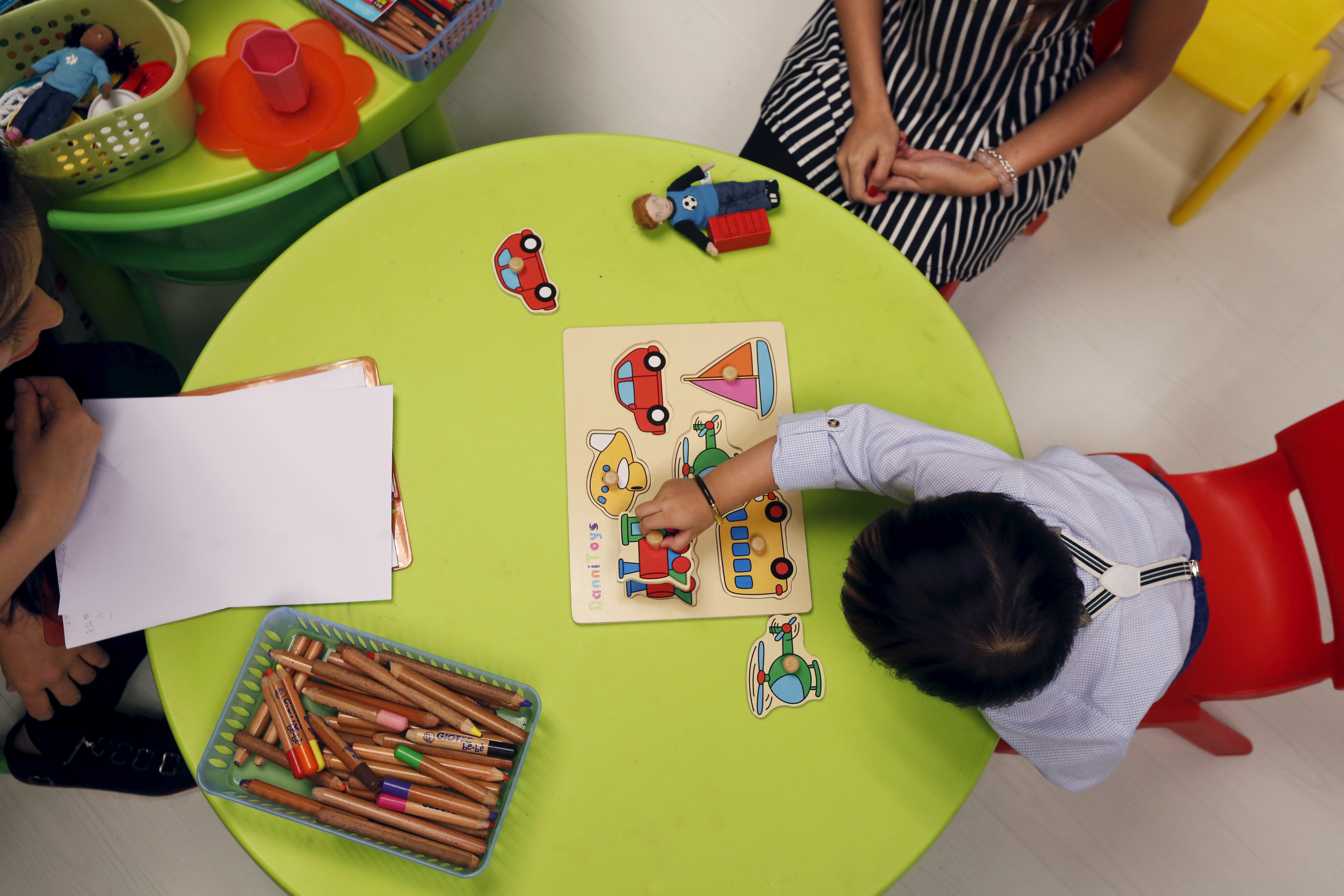 A toddler sitting at a round table indentifying objects placed in front of him