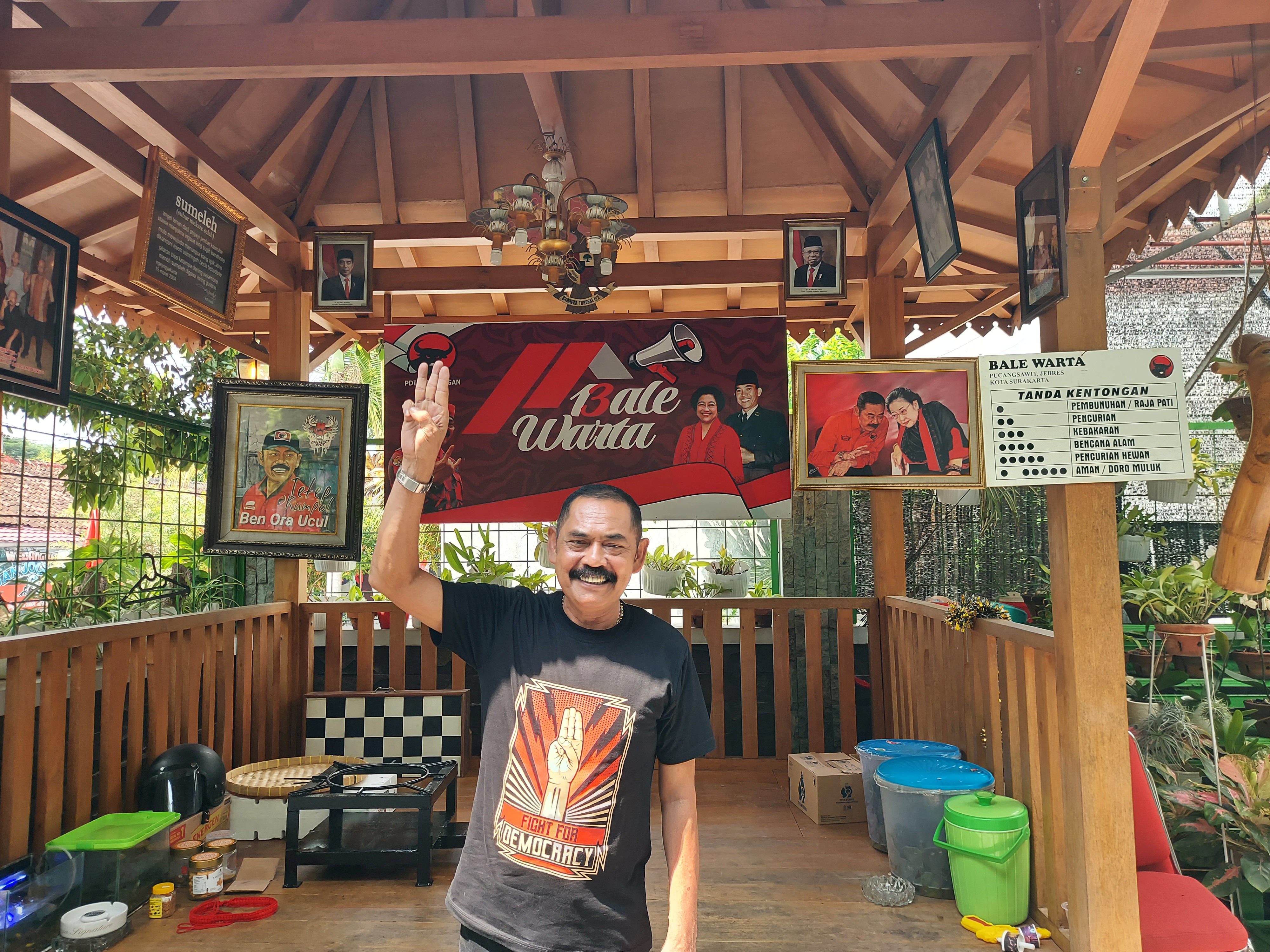 Fransiskus Xaverius Hadi Rudyatmo. He is outside a wooden open-sided building decorated with posters for the PDI-P. He is wearing a T-shirt saying 'Fight for Democracy' and featuring the three fingered salute