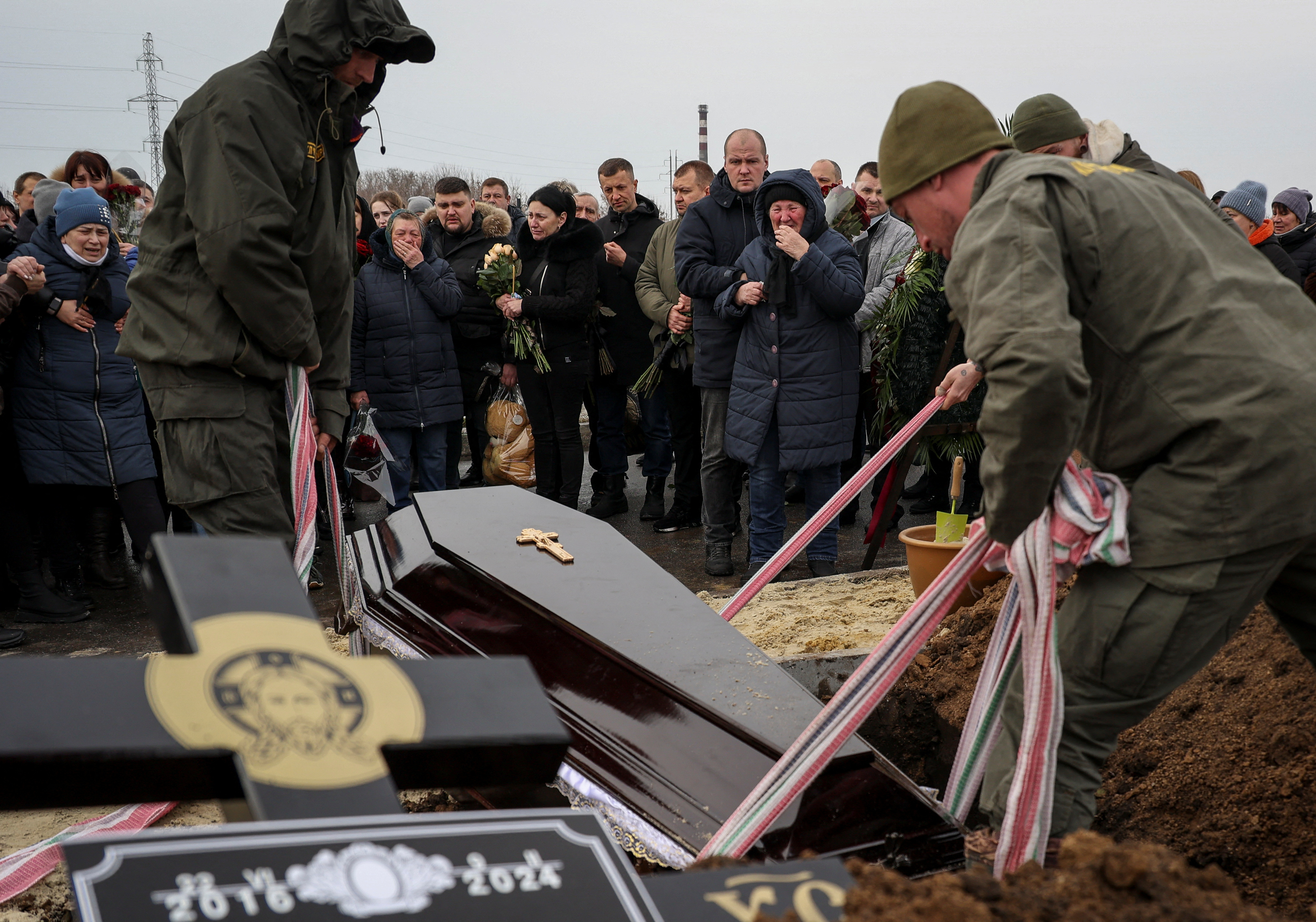 Relatives and friends look distraught as a coffin is lowered into the ground at a funeral for a family killed in a Russian attack on Kharkiv