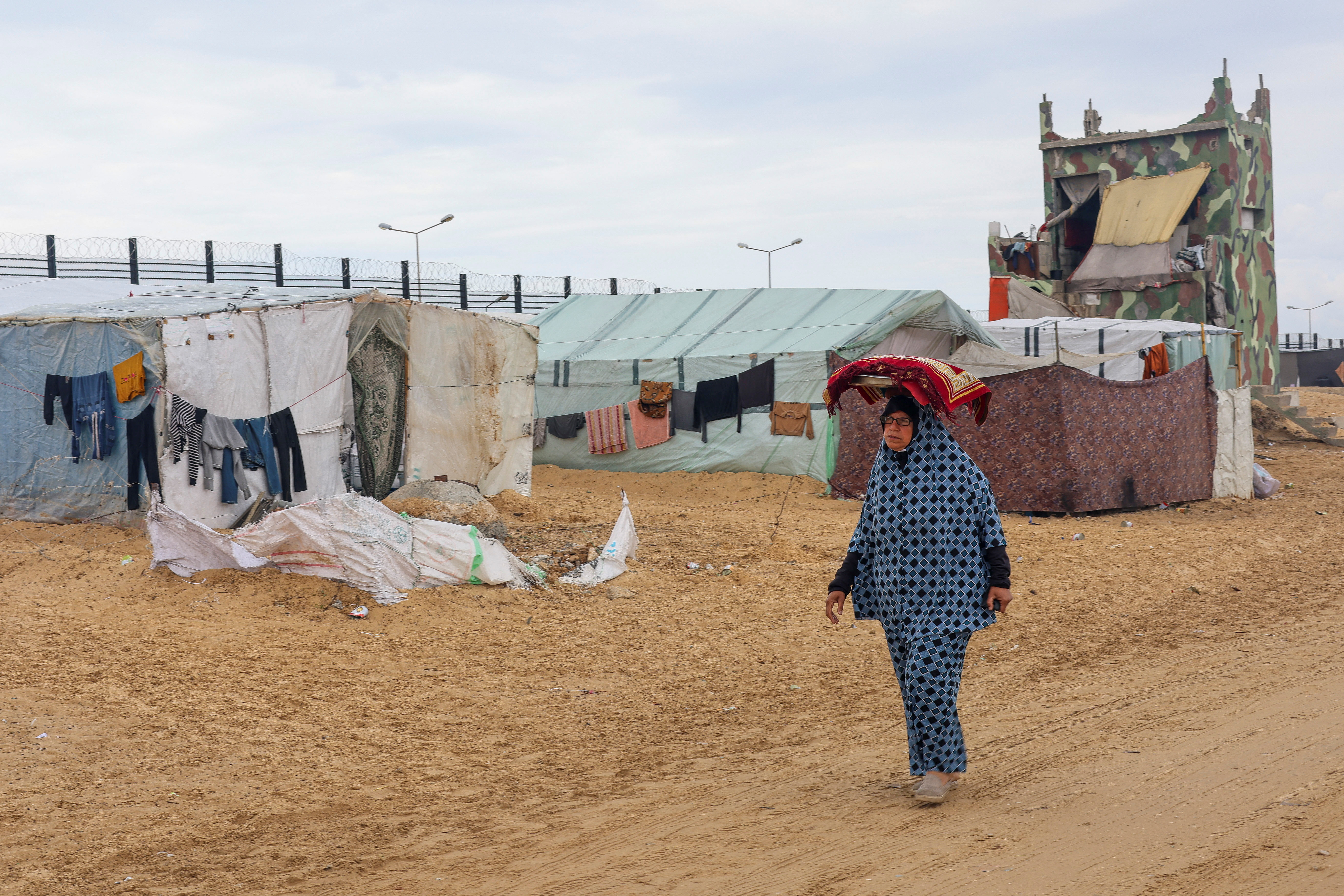 A displaced Palestinian woman, who fled her house due to Israeli strikes, amid the ongoing conflict between Israel and the Palestinian Islamist group Hamas, carries a tray with bread on her head as she walks past the border with Egypt, amid fears of an Israeli ground assault in Rafah, in the southern Gaza Strip February 18