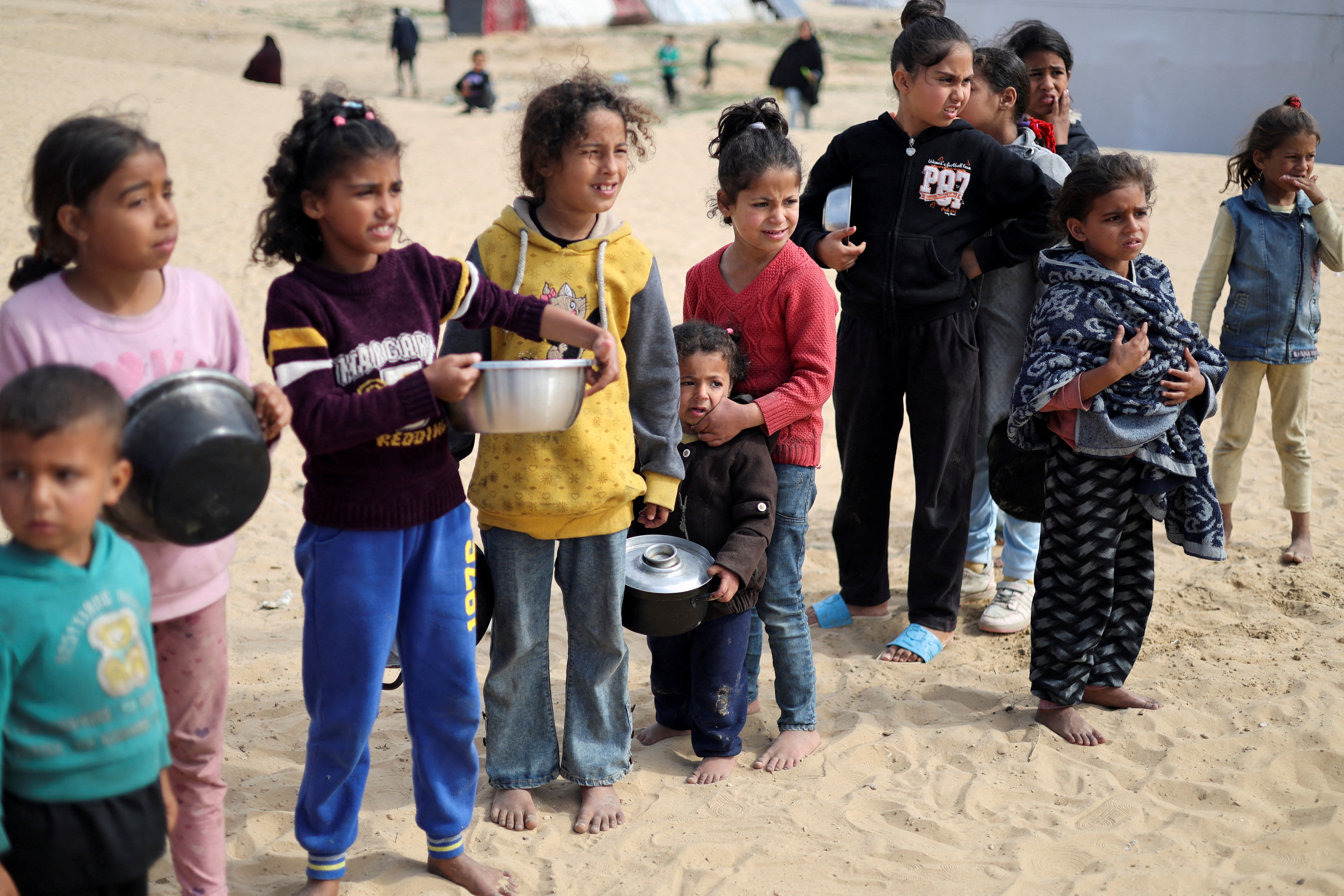 Displaced Palestinian children wait to receive free food at a tent camp, amid food shortages
