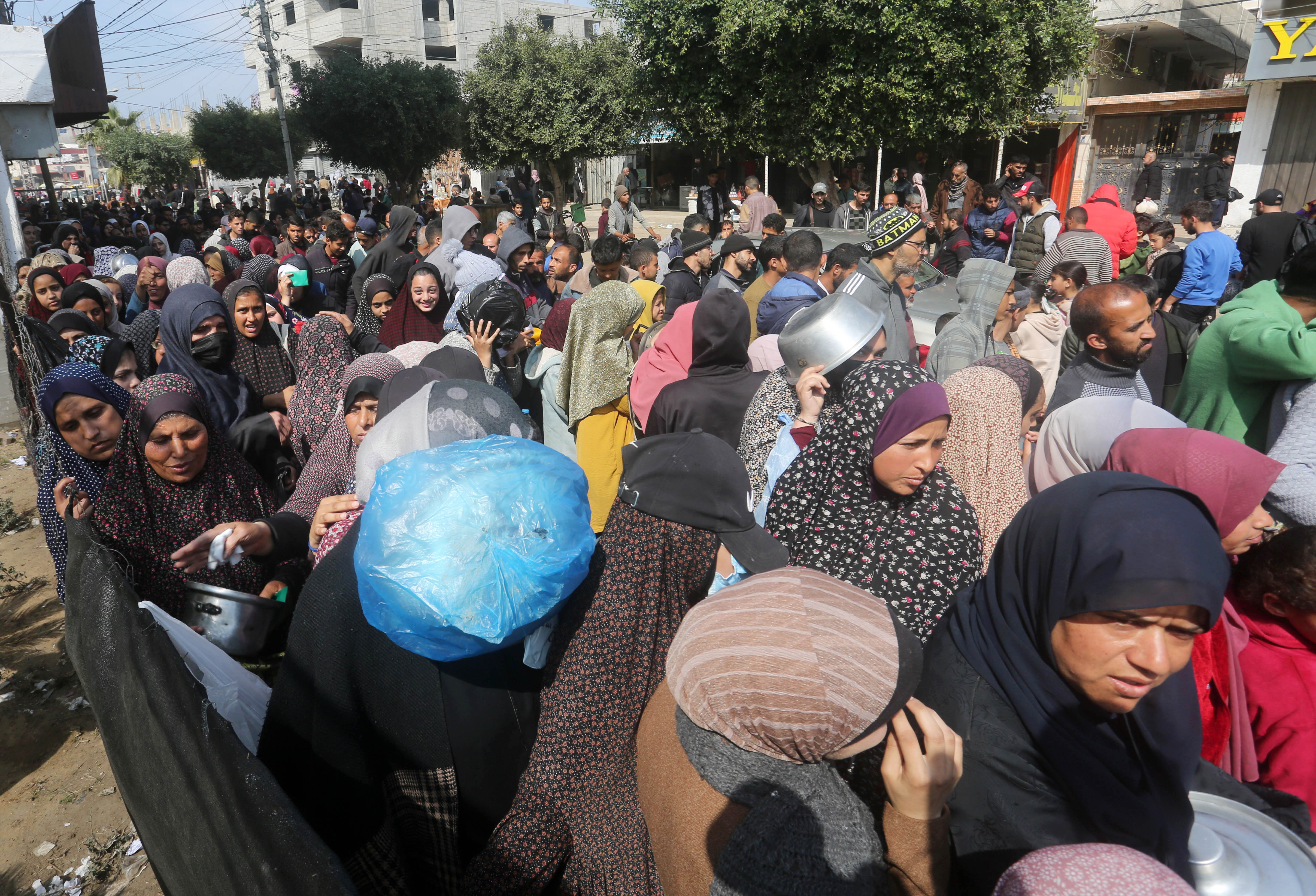 Palestinians, with empty containers wait in a line for food,