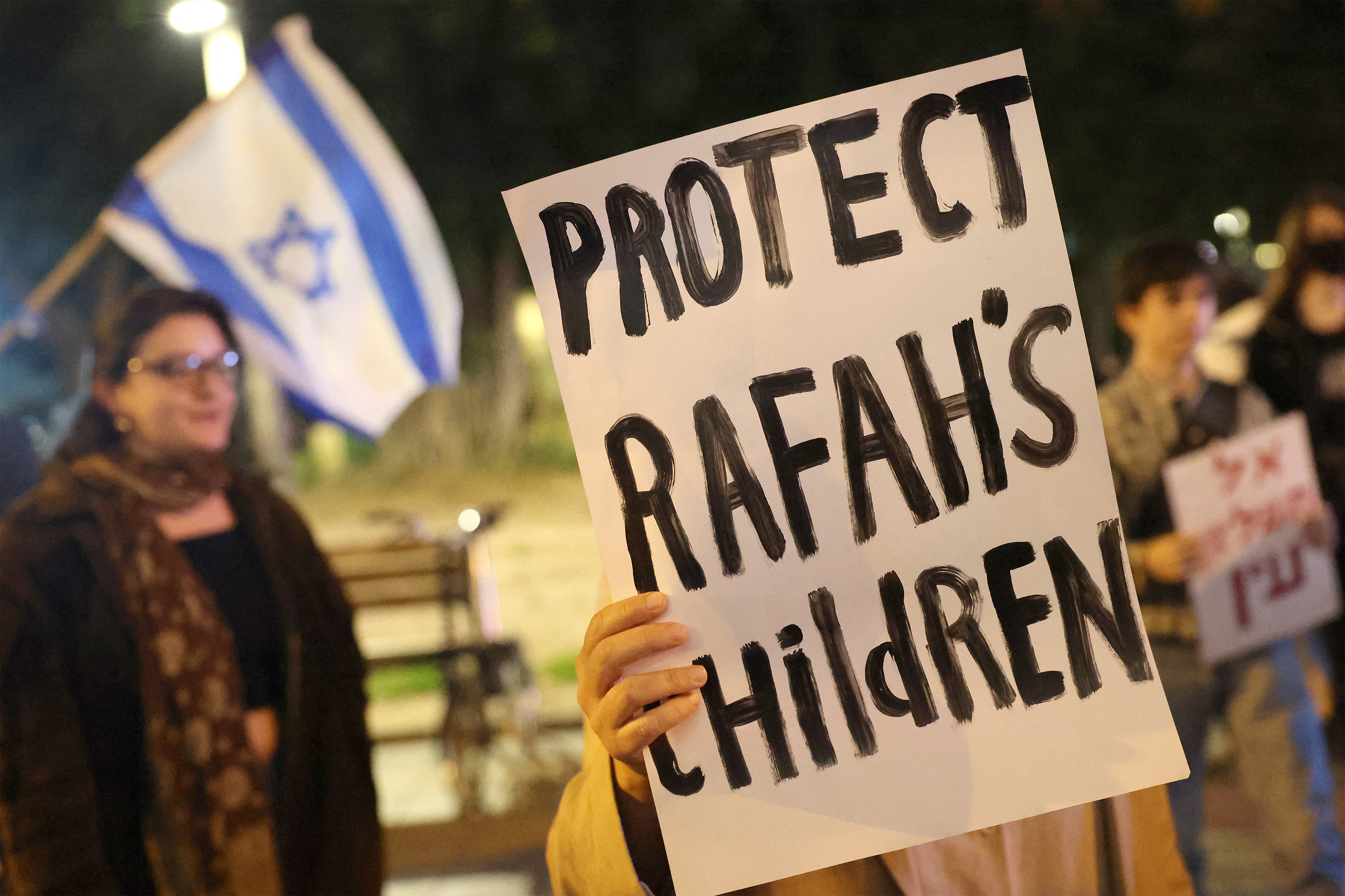 a sign says protect Rafah's children with an Israeli flag in the background
