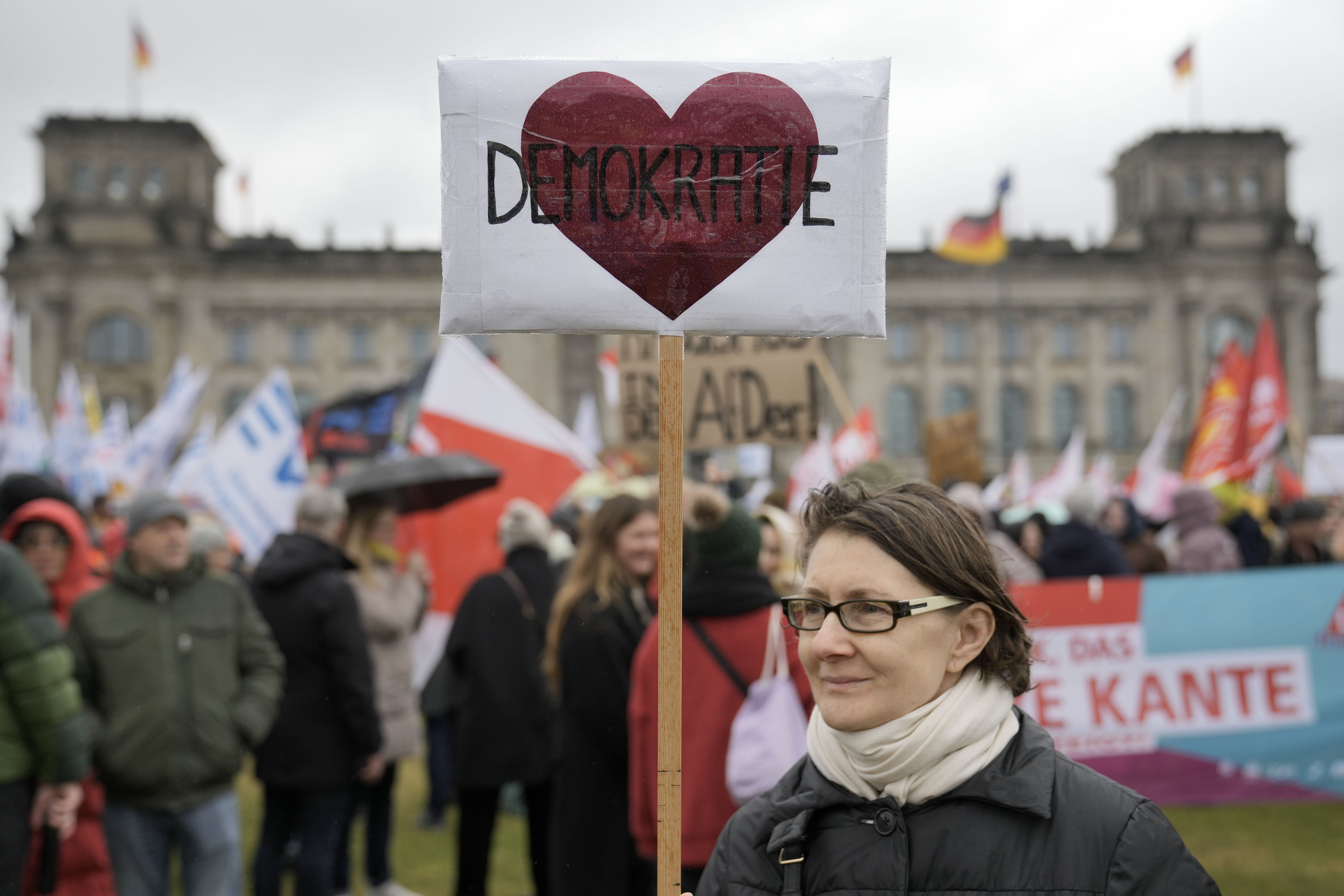 A protestor holds a sign reading 'Democracy' in front of Germany's parliament Reichstag during a demonstration against the AfD party and right-wing extremism in Berlin, Germany, Saturday, Feb. 3