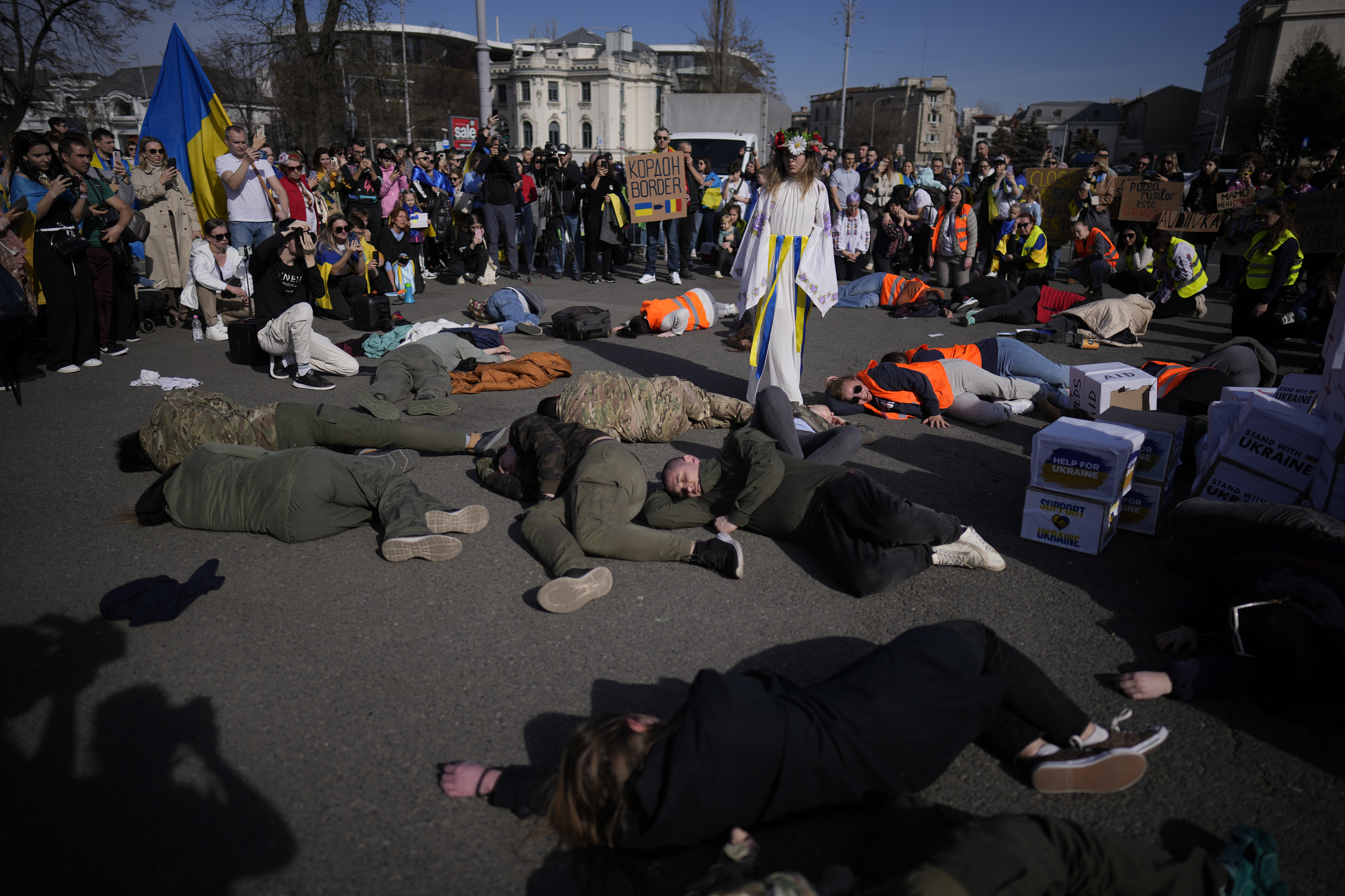 Ukrainians take part in an artistic moment portraying the life of Ukrainian civilians during war, outside the Victoria Palace, the Romanian government headquarters in Bucharest, Romania, Saturday, Feb. 24, 2024. Members of the Ukrainian community staged a march in the Romanian capital to mark the two year anniversary of the Russian invasion of Ukraine