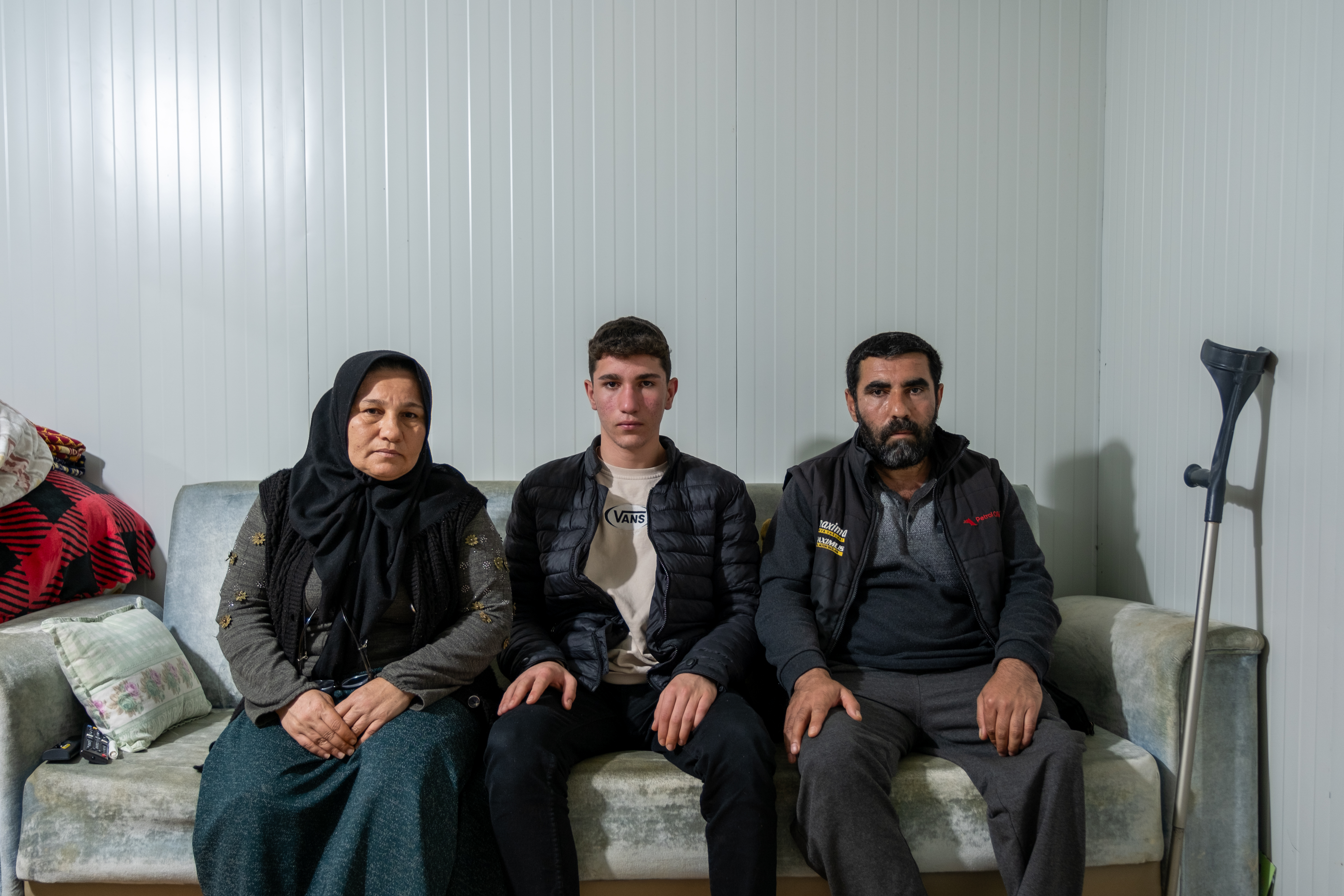 Adile Yetkin, left, Hasan Yetkin, right, and their son, Muhammet, 15, in their container home in Adiyaman. Both Adile and Hasan lost legs in the earthquake, and their eldest son was killed [Alaeddin Cogal/Al Jazeera]