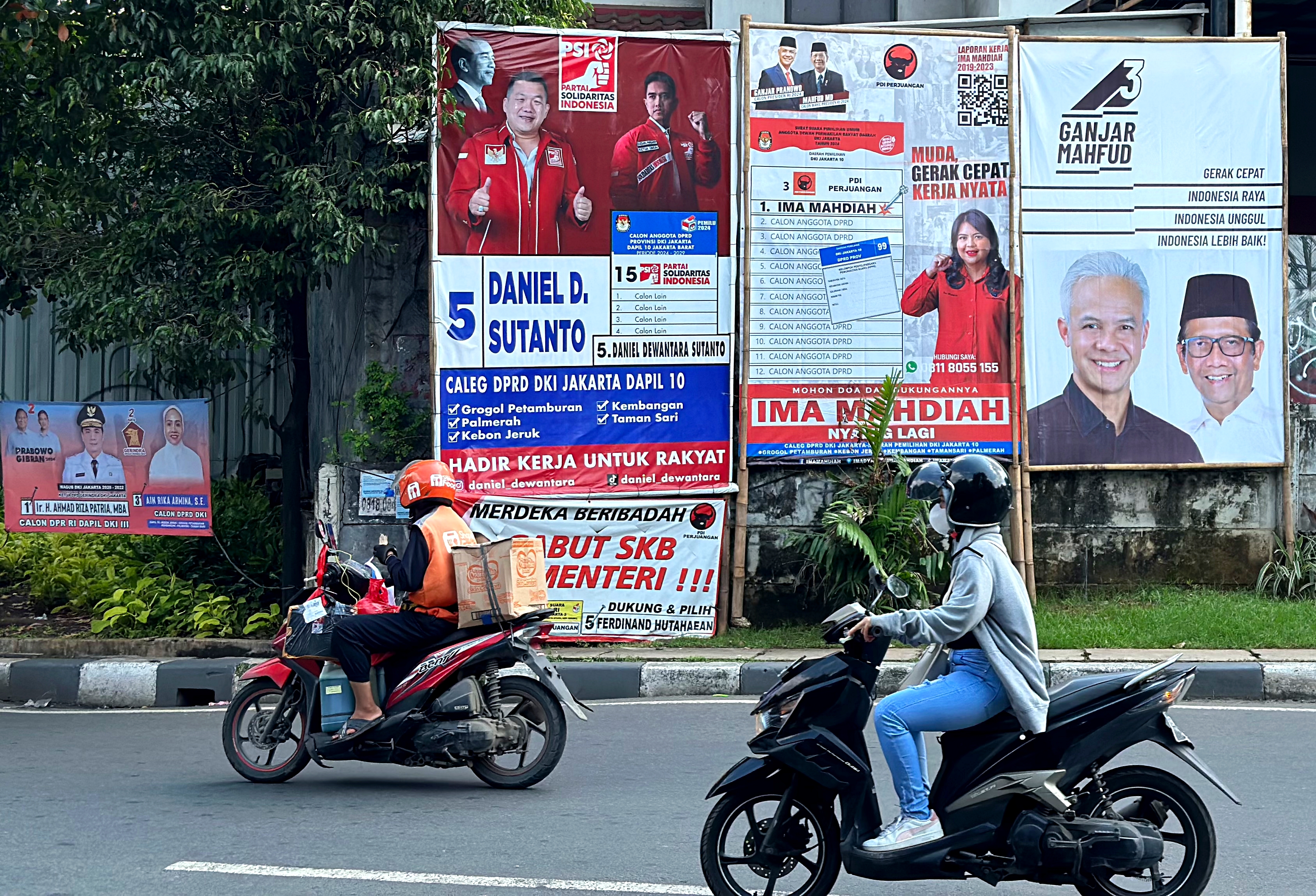 Motorcyclists drive past campaign banners for various candidates in Jakarta