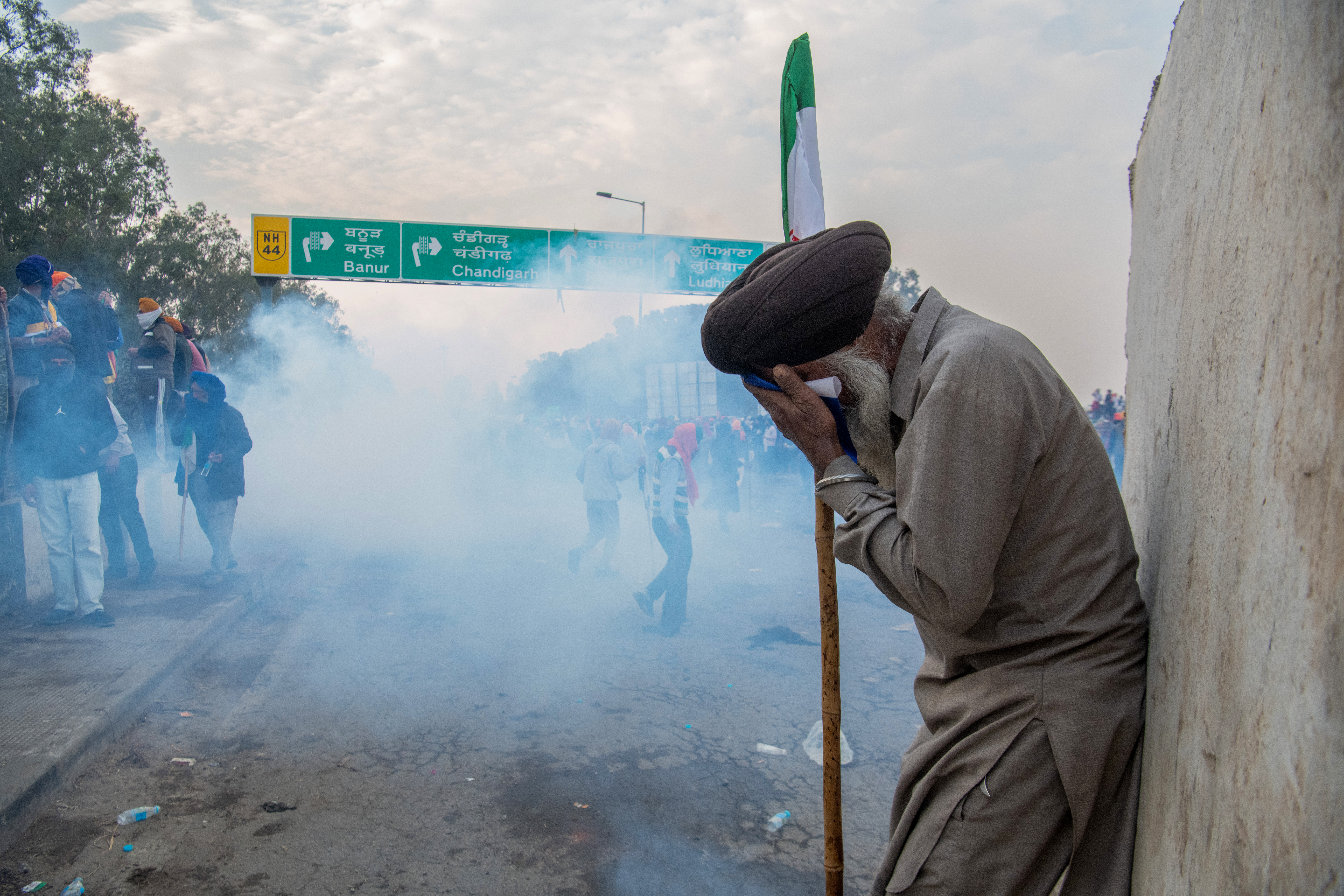 Shielding his eyes, a farmer protects himself from tear gas smoke at the Sandhu border, where police deployed tear gas shells and rubber bullets to scatter protesting farmers striving to advance towards New Delhi to voice their demands.