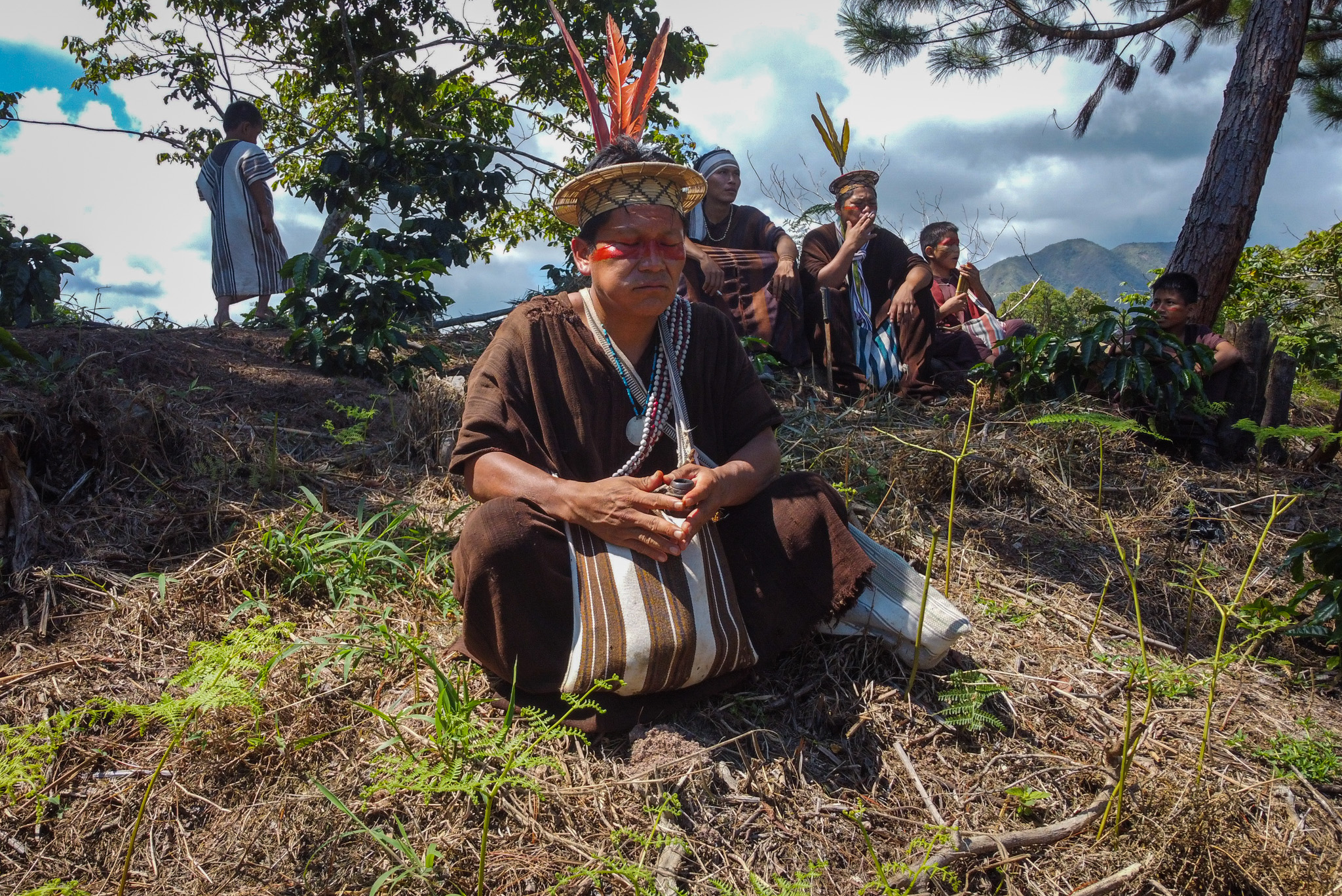 Ashaninka leader Tsitsiri Samaniego sits crosslegged on a hillside, with his family in the background.