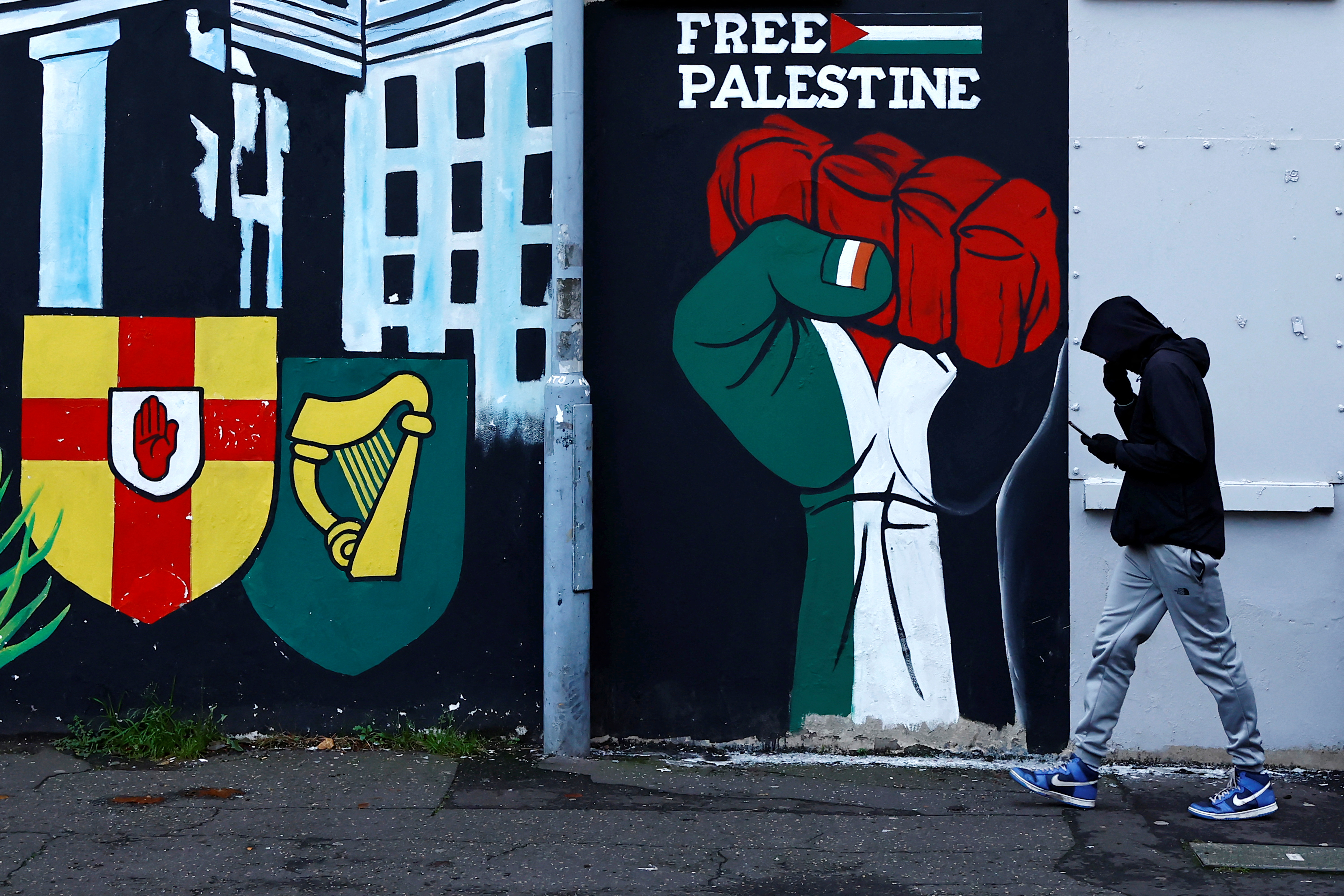 A man walks past a mural in solidarity with Palestinians in Gaza, amid the ongoing conflict between Israel and Hamas, in the Nationalist area along the Falls Road in Belfast, Northern Ireland