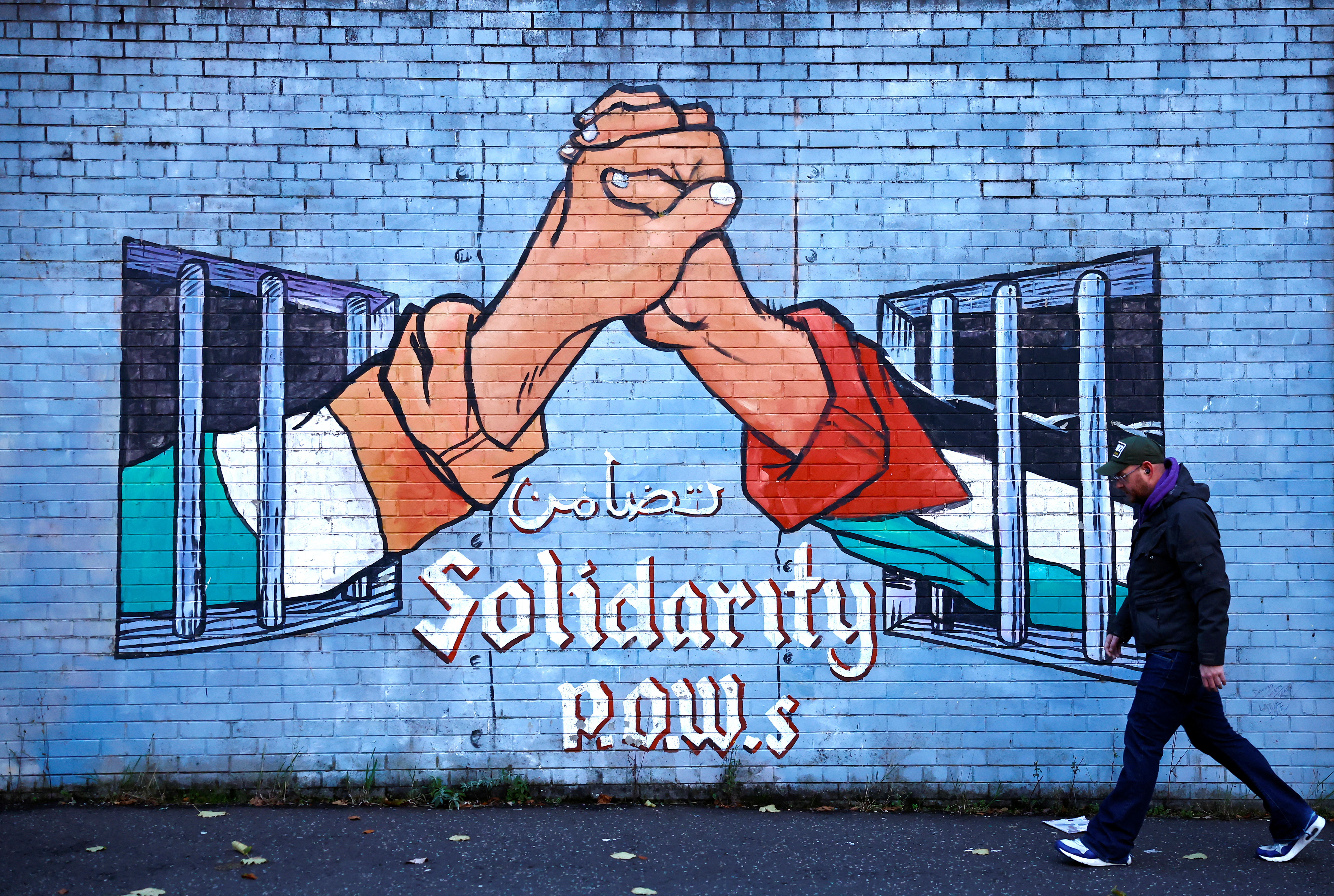 A man walks past a mural in solidarity with Palestinians in Gaza, amid the ongoing conflict between Israel and Hamas, in the Nationalist area along the International Wall on the Falls Road in Belfast, Northern Ireland