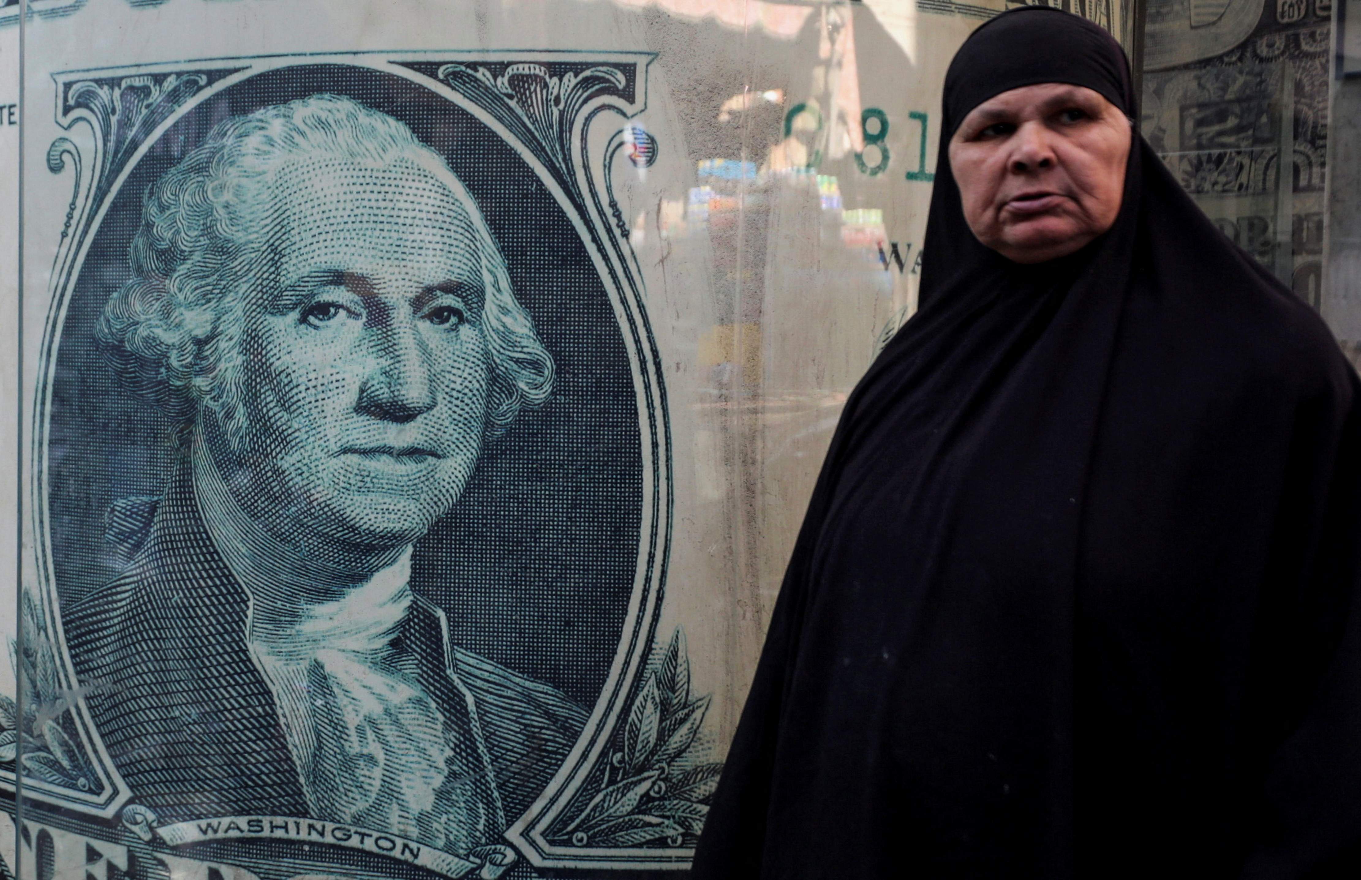 A woman stands next to a currency exchange point, displaying an image of the U.S. dollar, in Cairo, Egypt