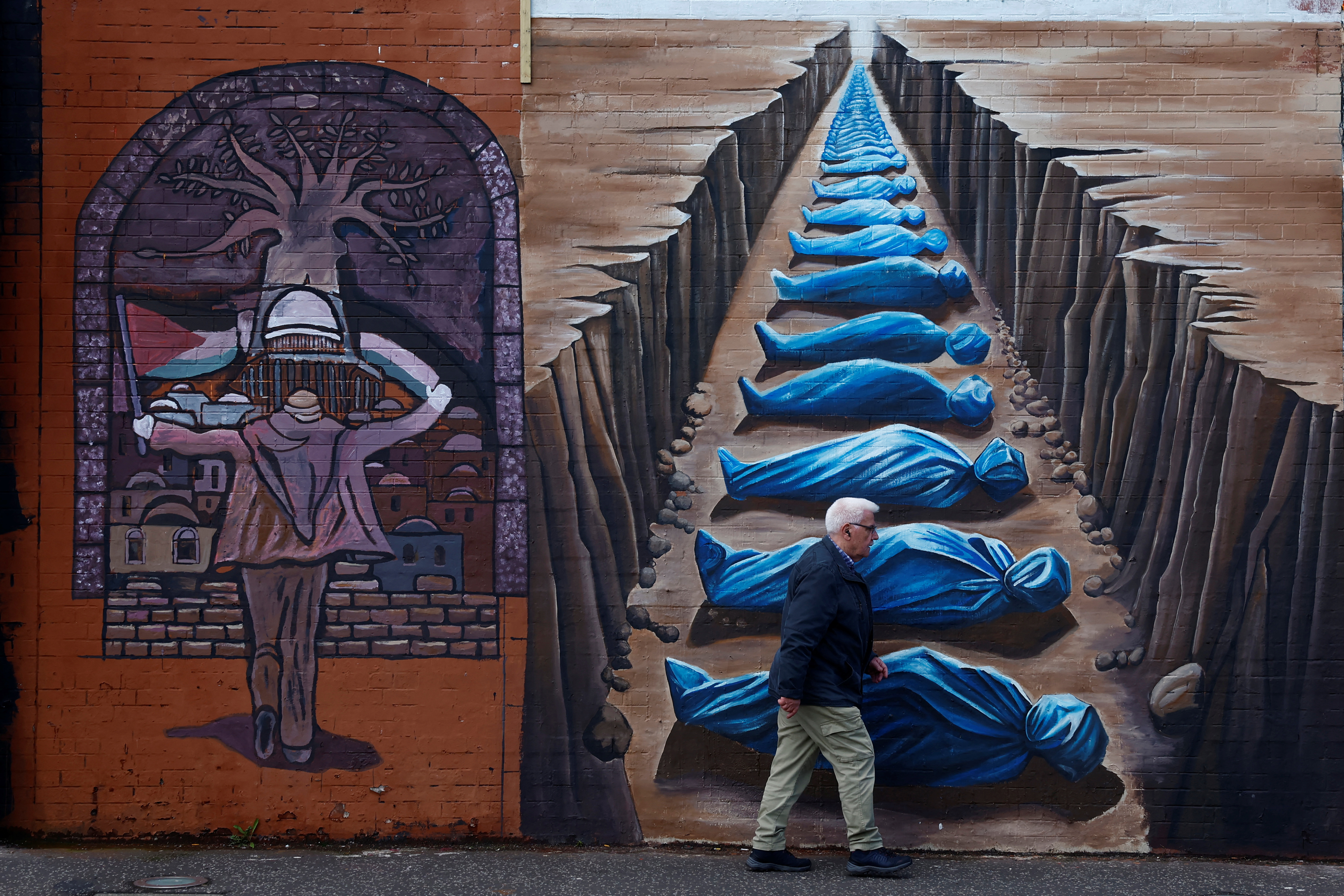 A man walks past pro-Palestinian murals on the International Wall in support of Gaza, amid the ongoing conflict between Israel and the Palestinian Islamist group Hamas, in Belfast, Northern Ireland, March 29