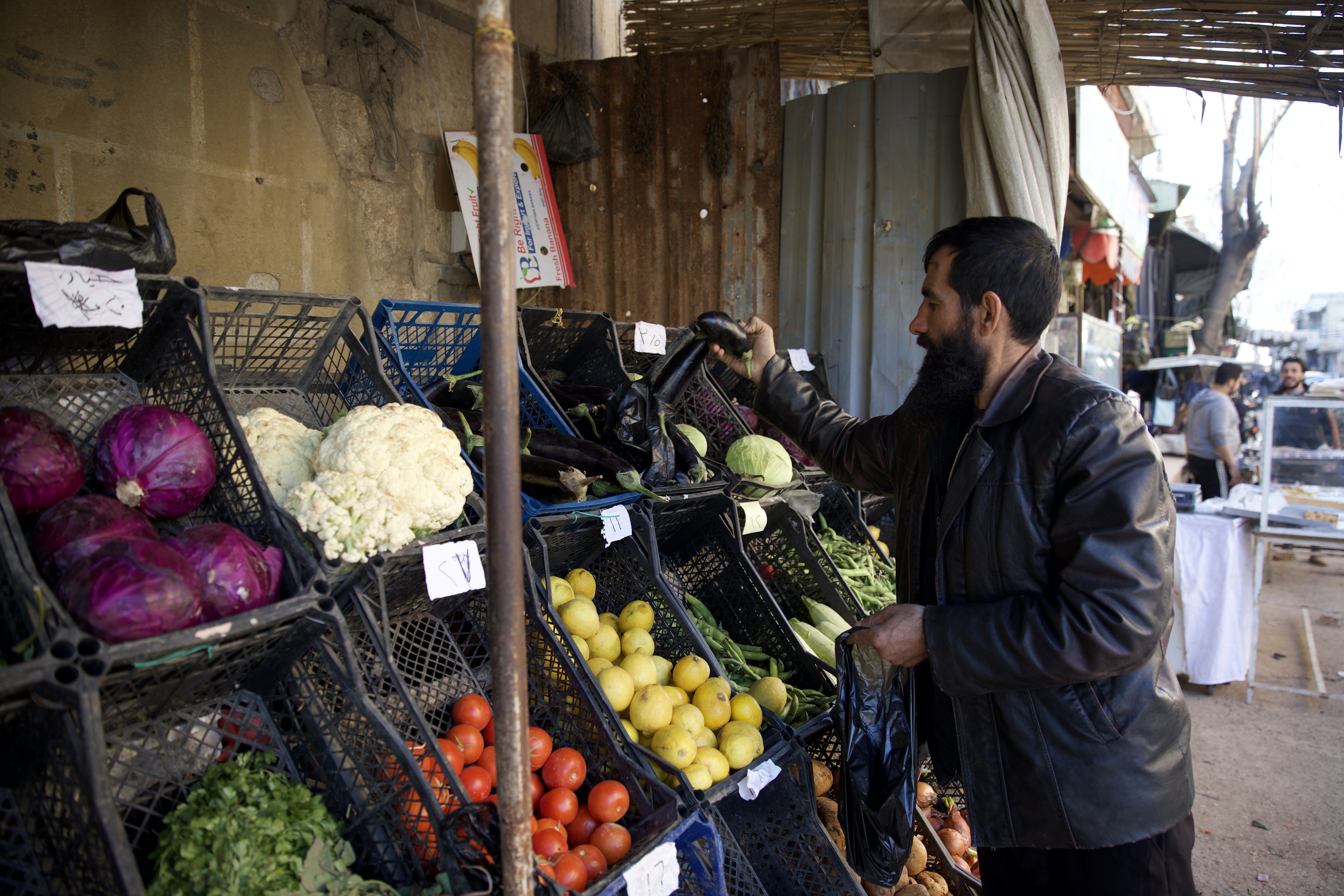 Khalid, a gentle, bearded man, picks out vegetables from a simple stand in the market