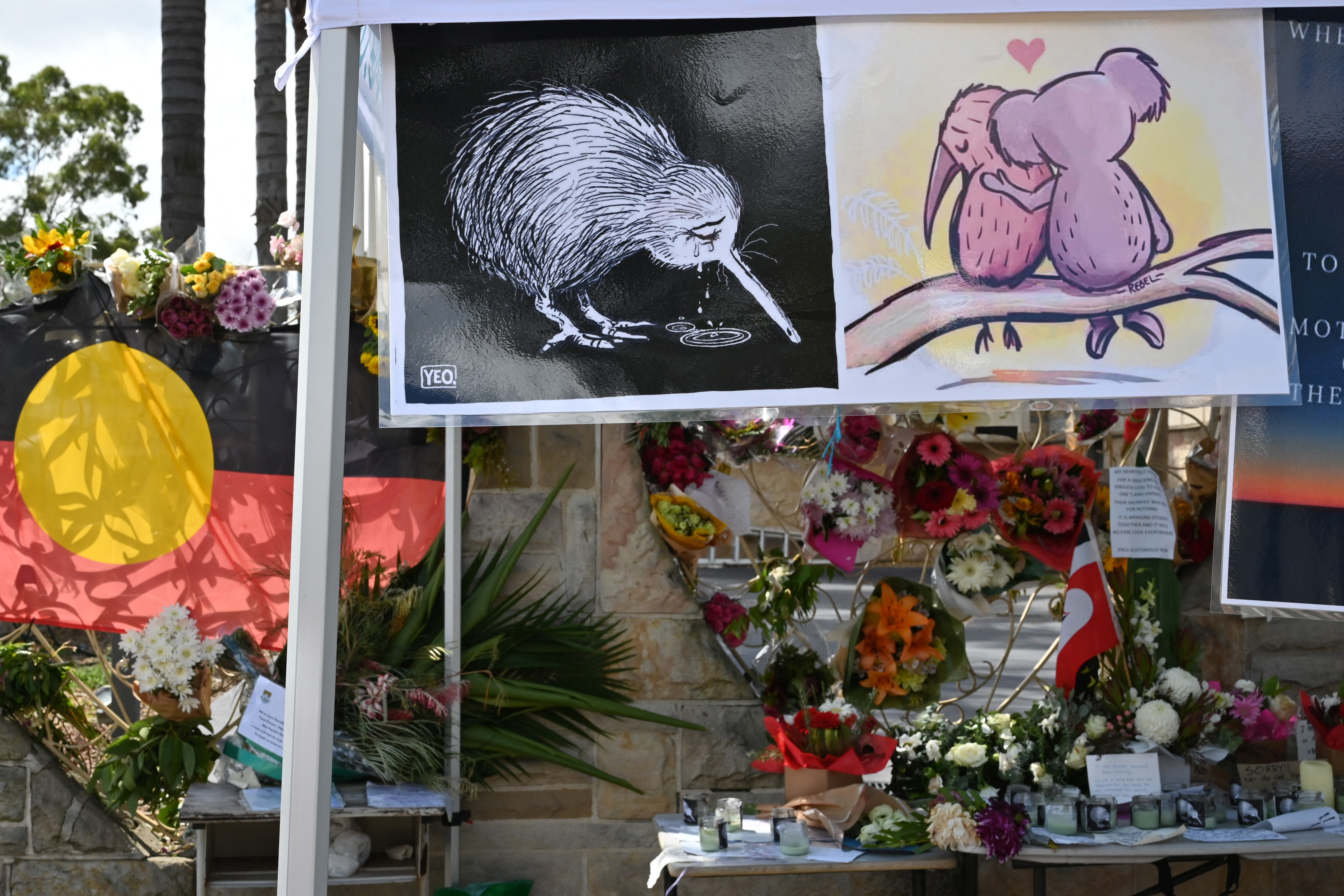 pictures at a memorial site filled with flowers show a kiwi bird and a koala hugging