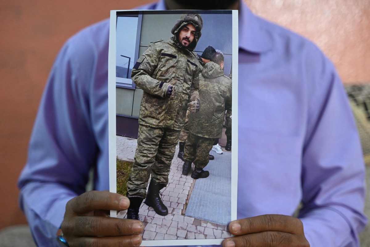 This photo taken on February 22, 2024 shows a picture printout of Indian national Mohammed Asfan, seen wearing Russian military fatigues who last called family from the southern Russian city of Rostov-on-Don before being deployed amid the conflict in Ukraine, being held by his brother Mohammed Imran in Hyderabad.