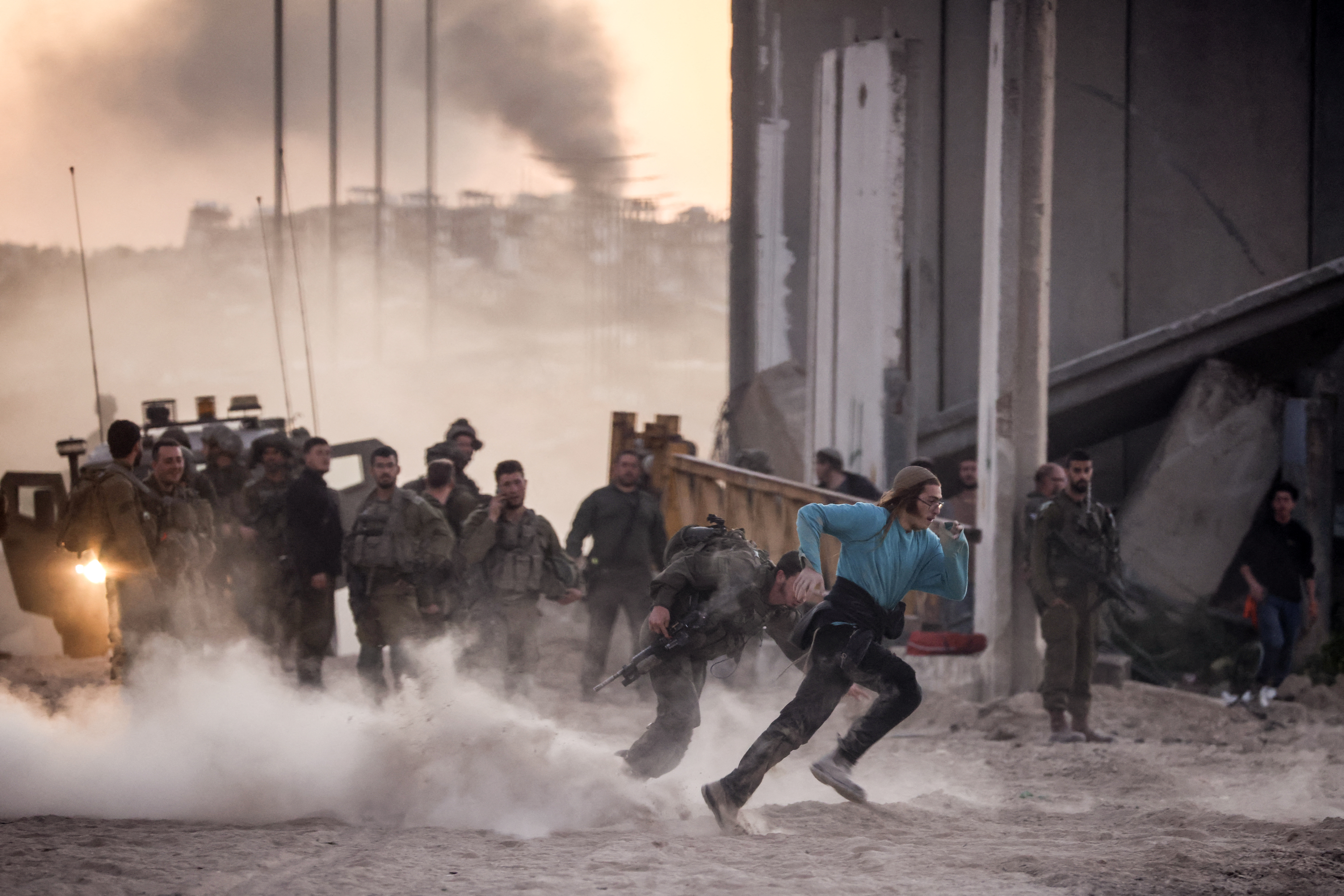 Smoke rises above the Gaza Strip from Israeli bombardment as an Israeli right wing activist runs during scuffles with Israeli troop near the Erez crossing, during a rally calling for the building of Israeli settlements in Gaza, on February 29, 2024, amid ongoing battles between Israel and the Palestinian militant group Hamas. (Photo by Oren ZIV / AFP)