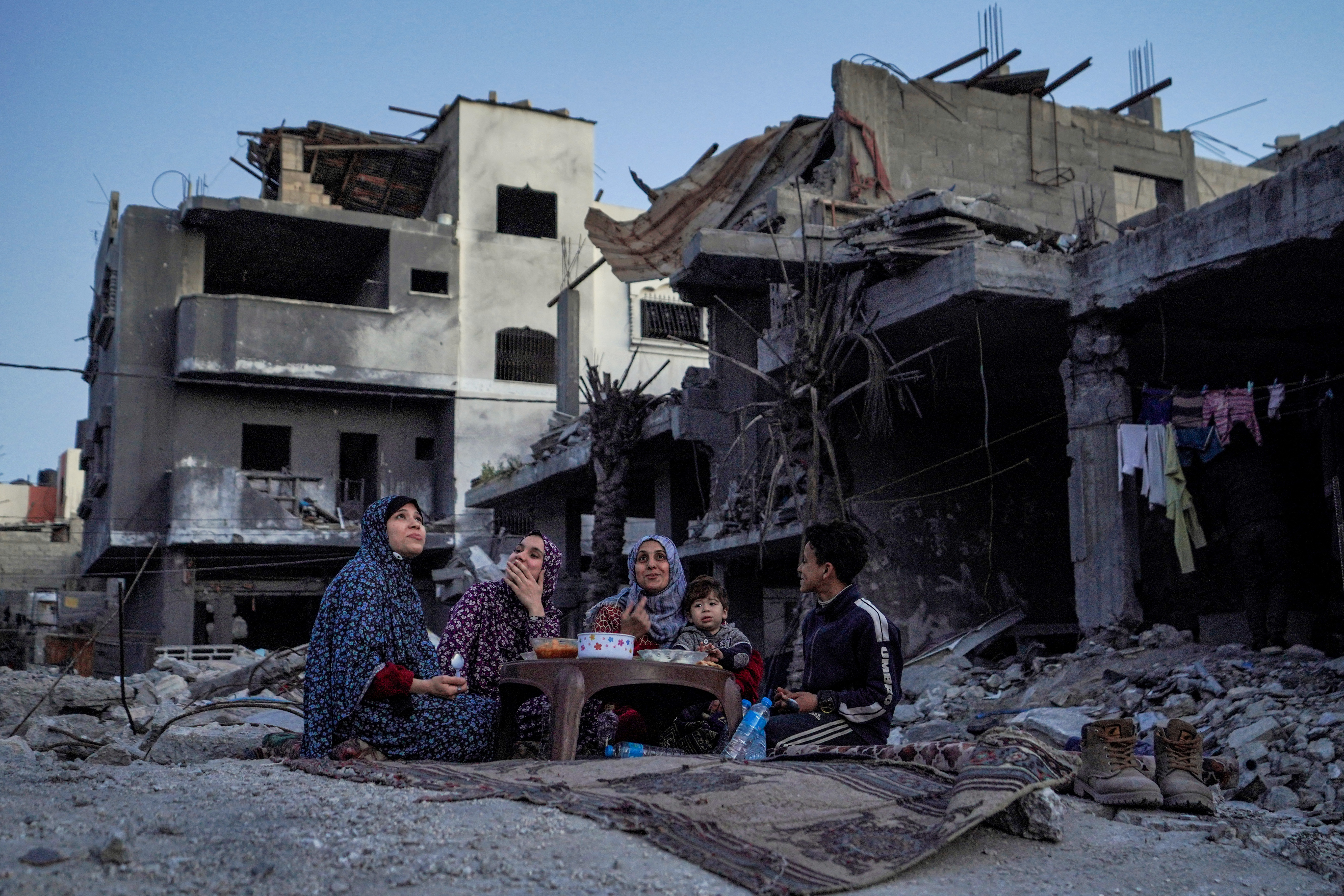 The Palestinian Al-Naji family eats an iftar meal, the breaking of fast, amidst the ruins of their family house, on the first day of the Muslim holy fasting month of Ramadan, in Deir el-Balah in the central Gaza Strip on March 11
