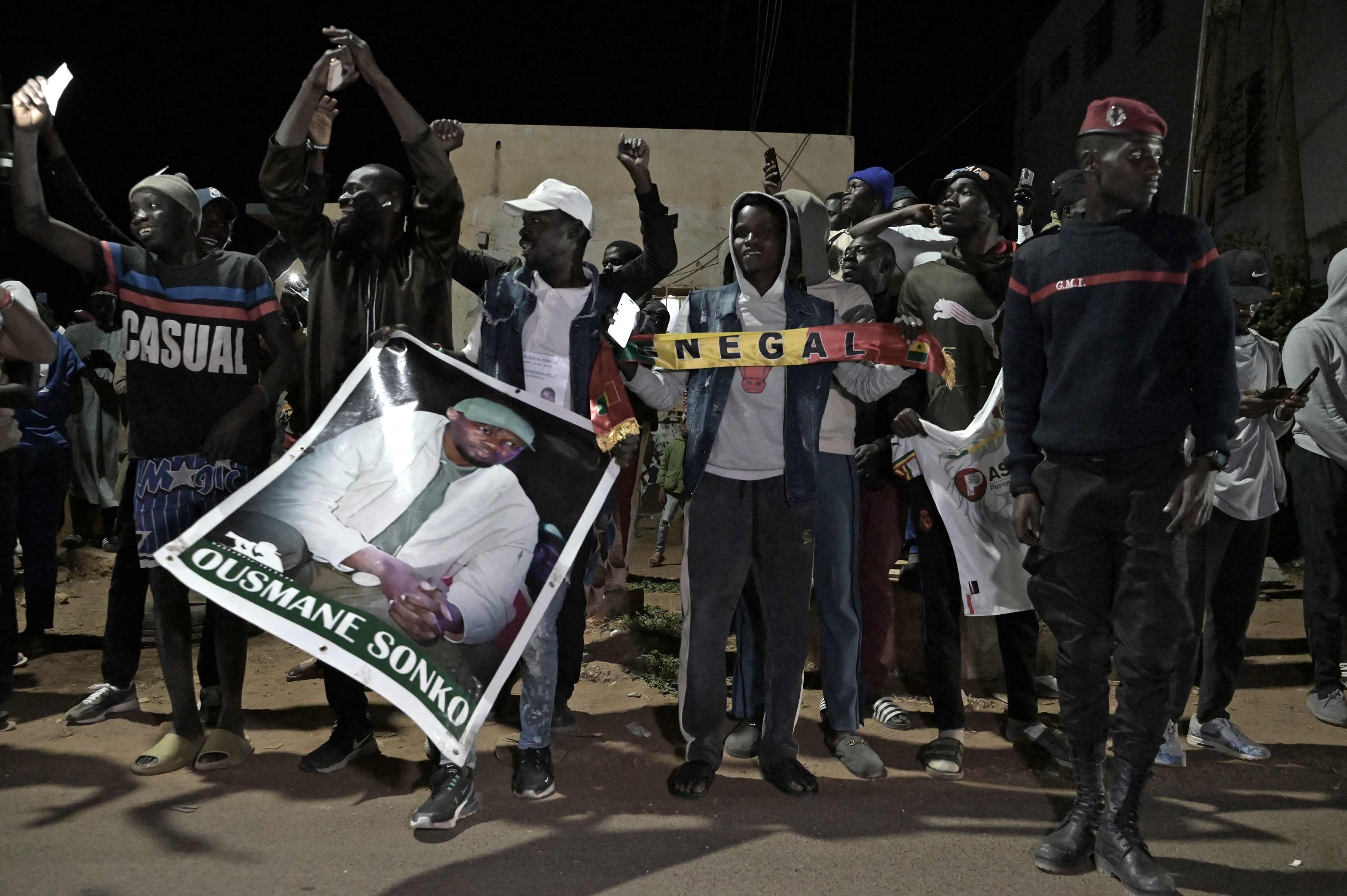 People celebrate the release of Senegalese opposition leader Ousmane Sonko and ally Bassirou Diomaye Faye. They are holding pictures of the men, and a banner reading SENEGAL. They look happy.