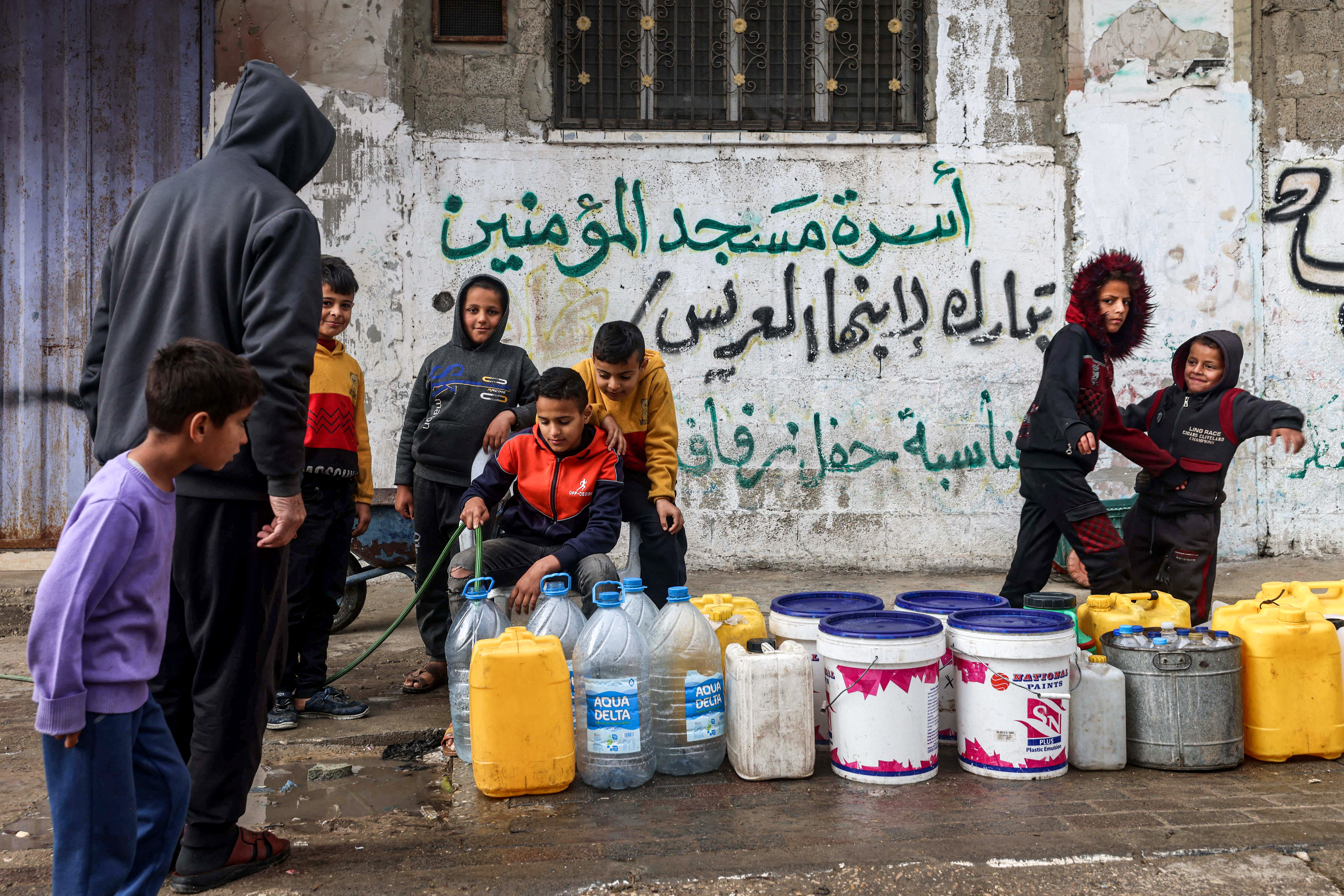 A boy fills water containers from a hose in Rafah