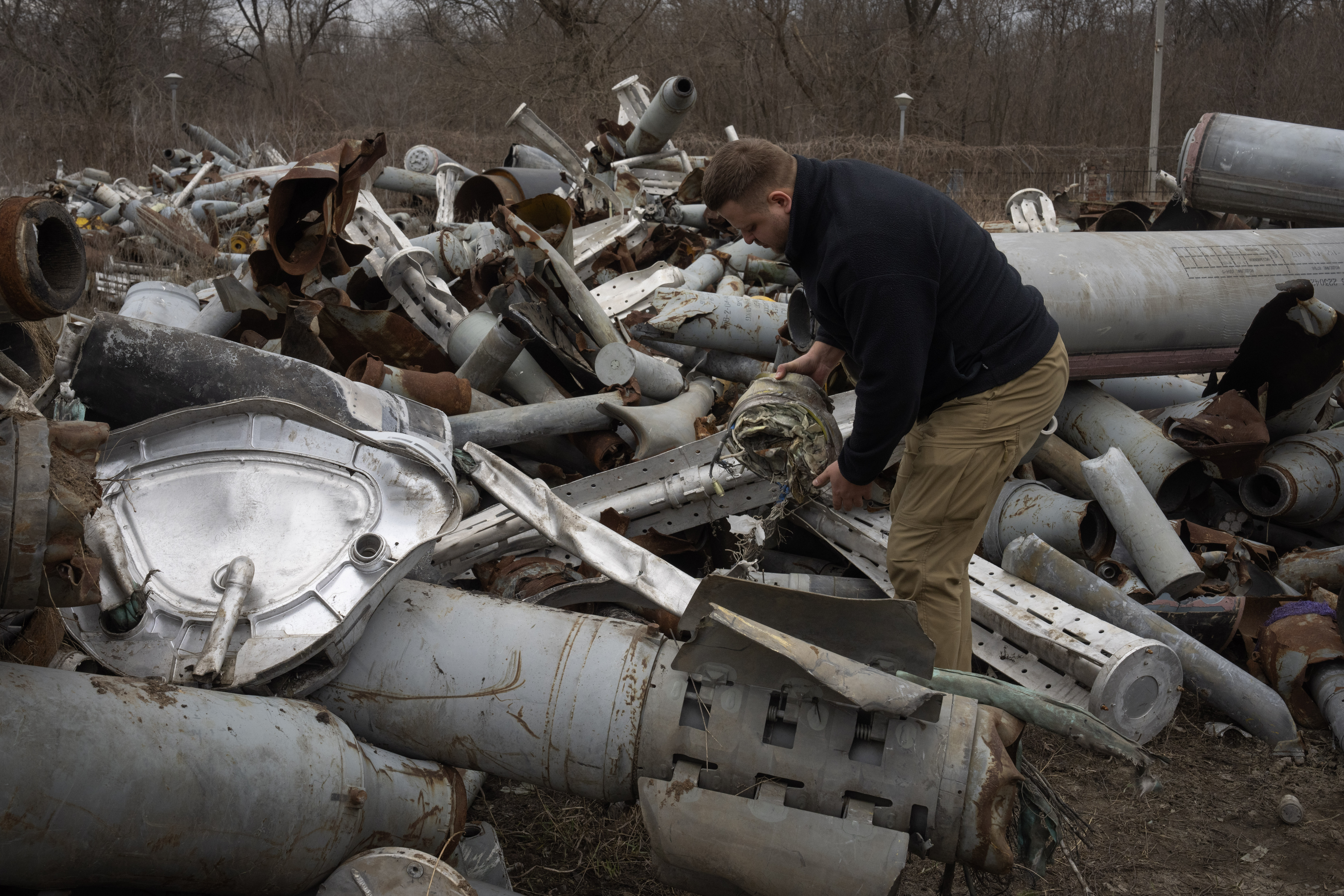 A Ukrainian investigator examining parts of Russian weapons fired at Ukraine. The missiles are of all sizes.